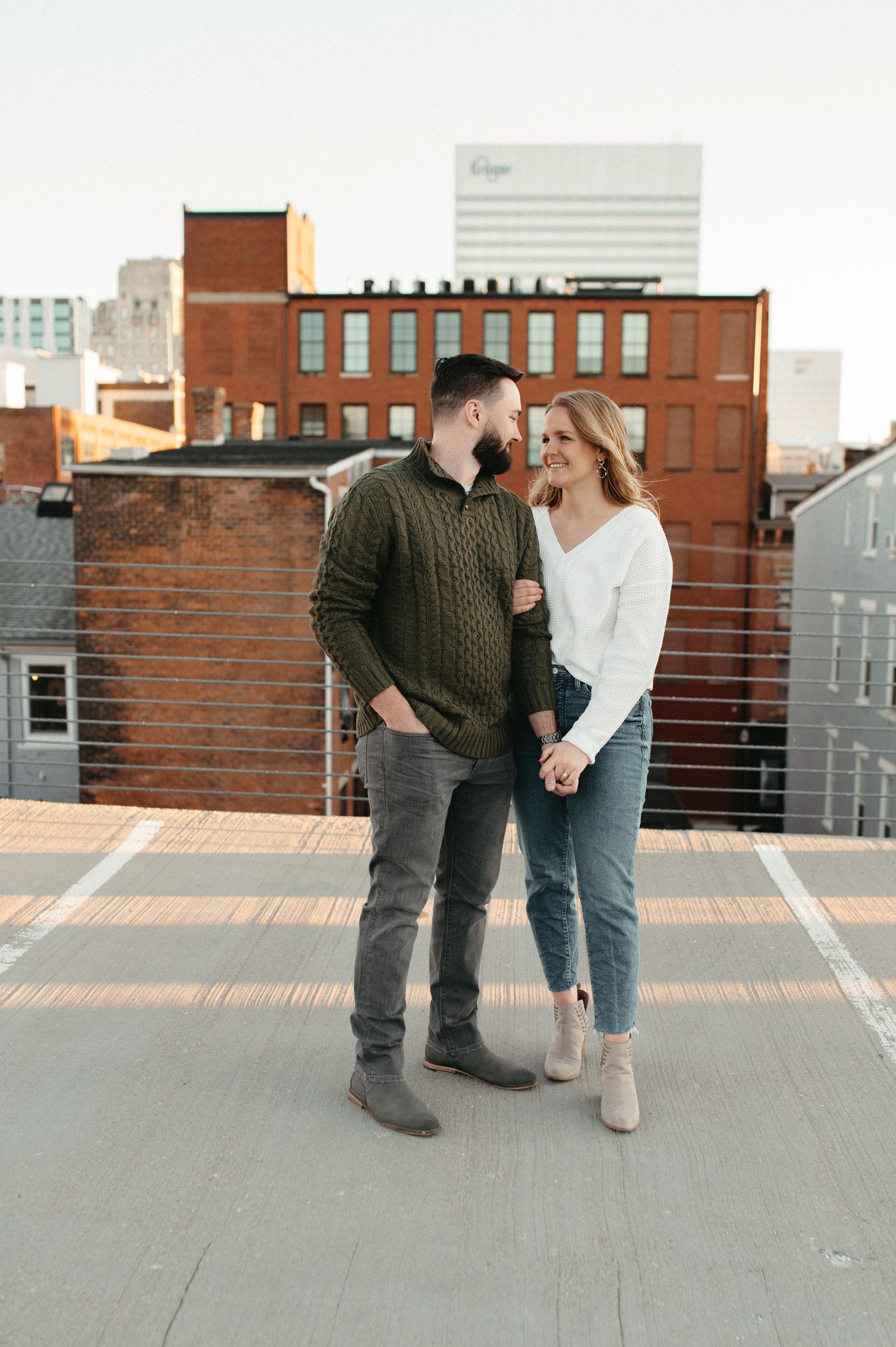 Two people laugh together while standing on a rooftop parking deck during golden hour.