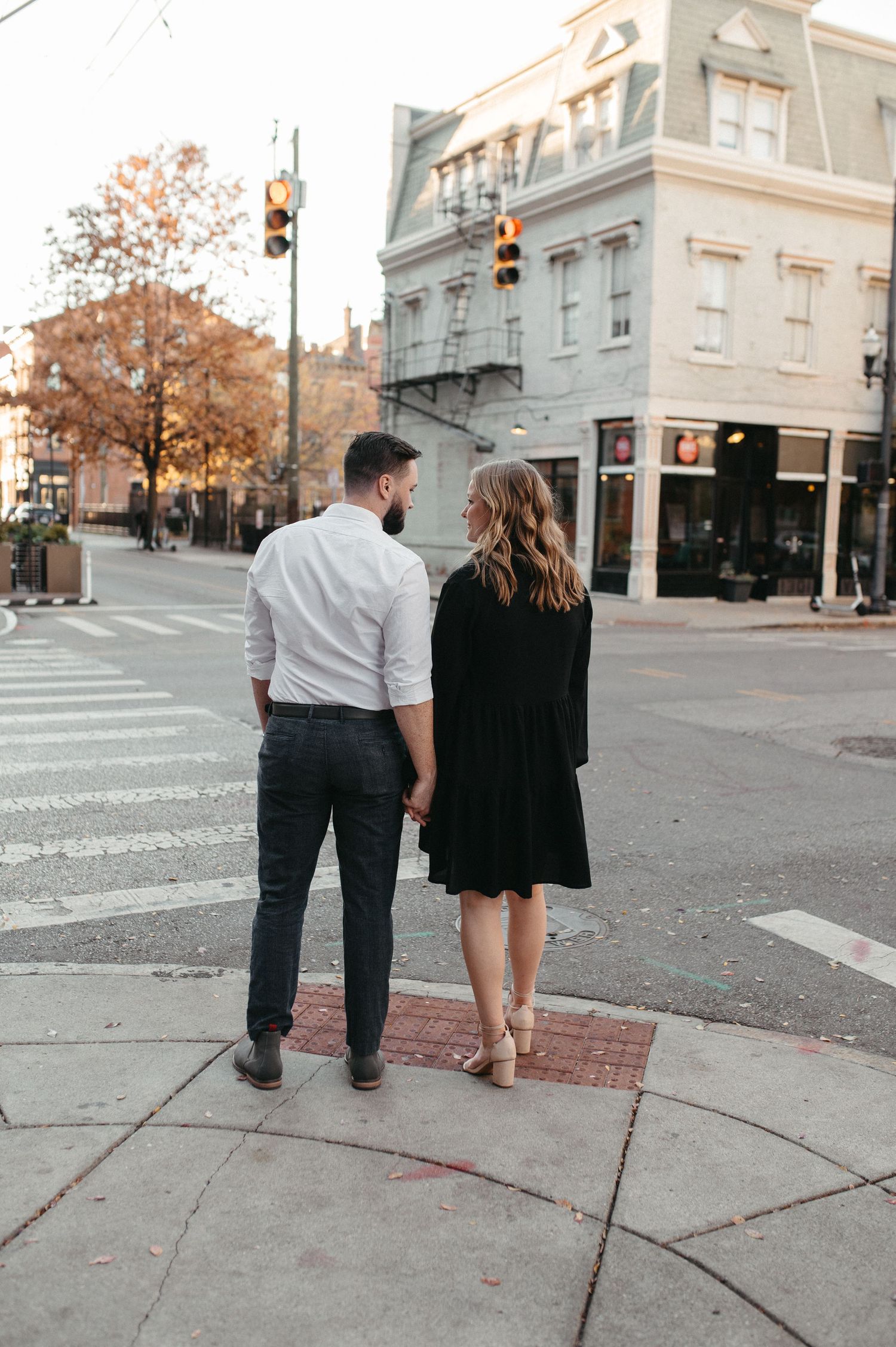 Couple walking hand in hand on downtown sidewalk during fall season.