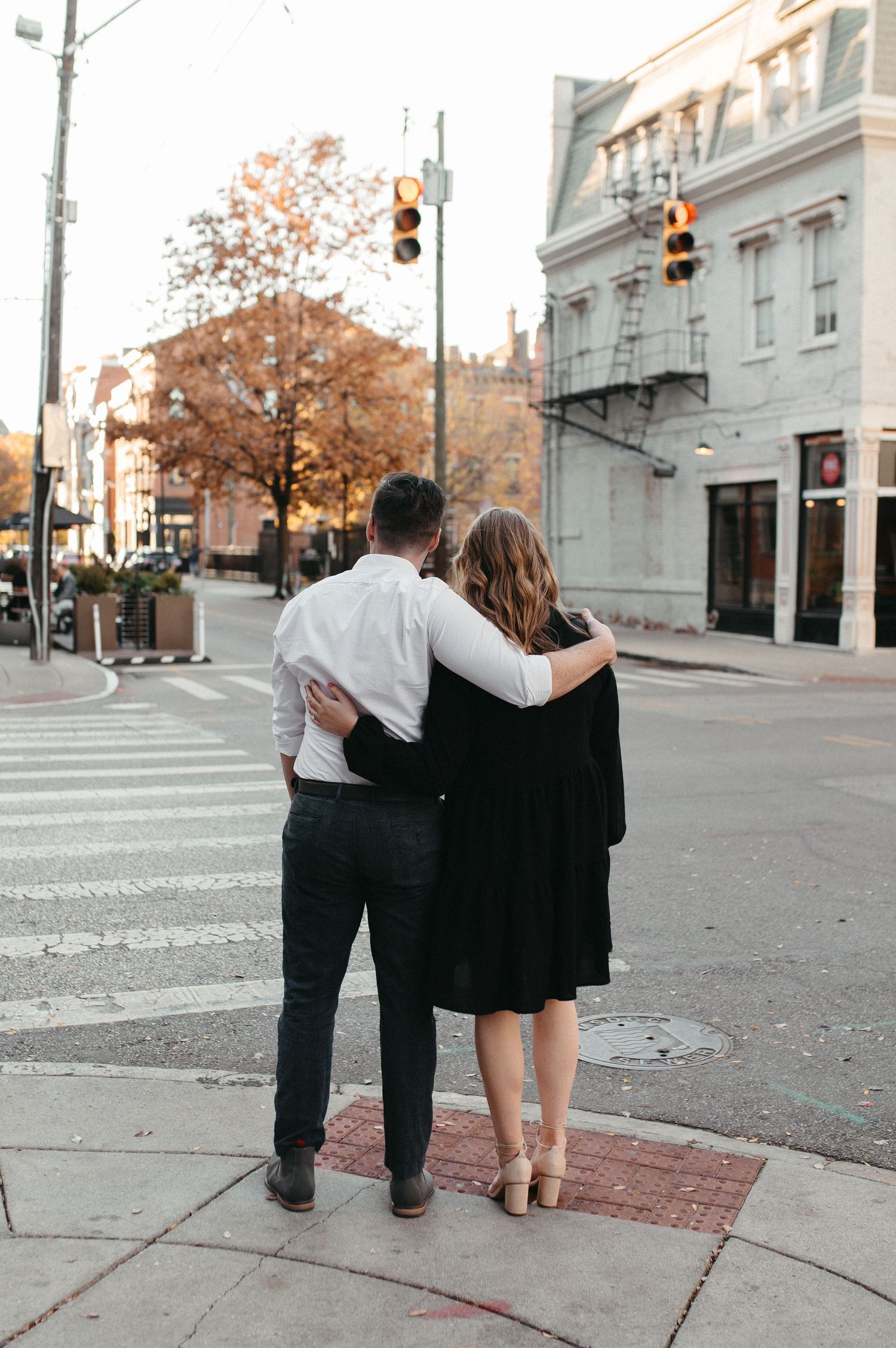 Couple embracing while standing on city corner with historic building in background.