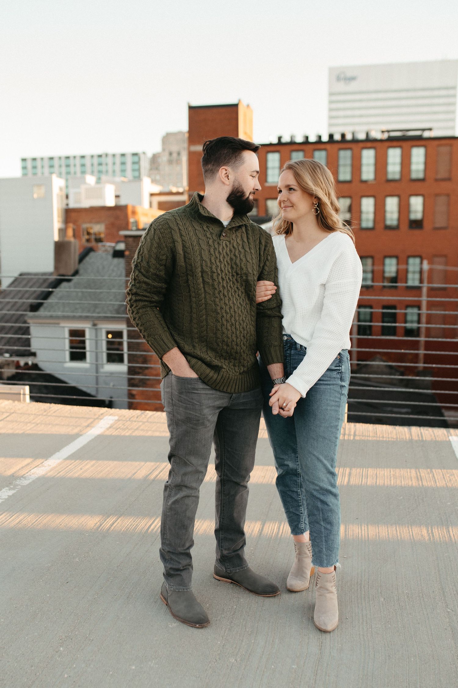 Couple in casual sweaters sharing a laugh together on a city rooftop.