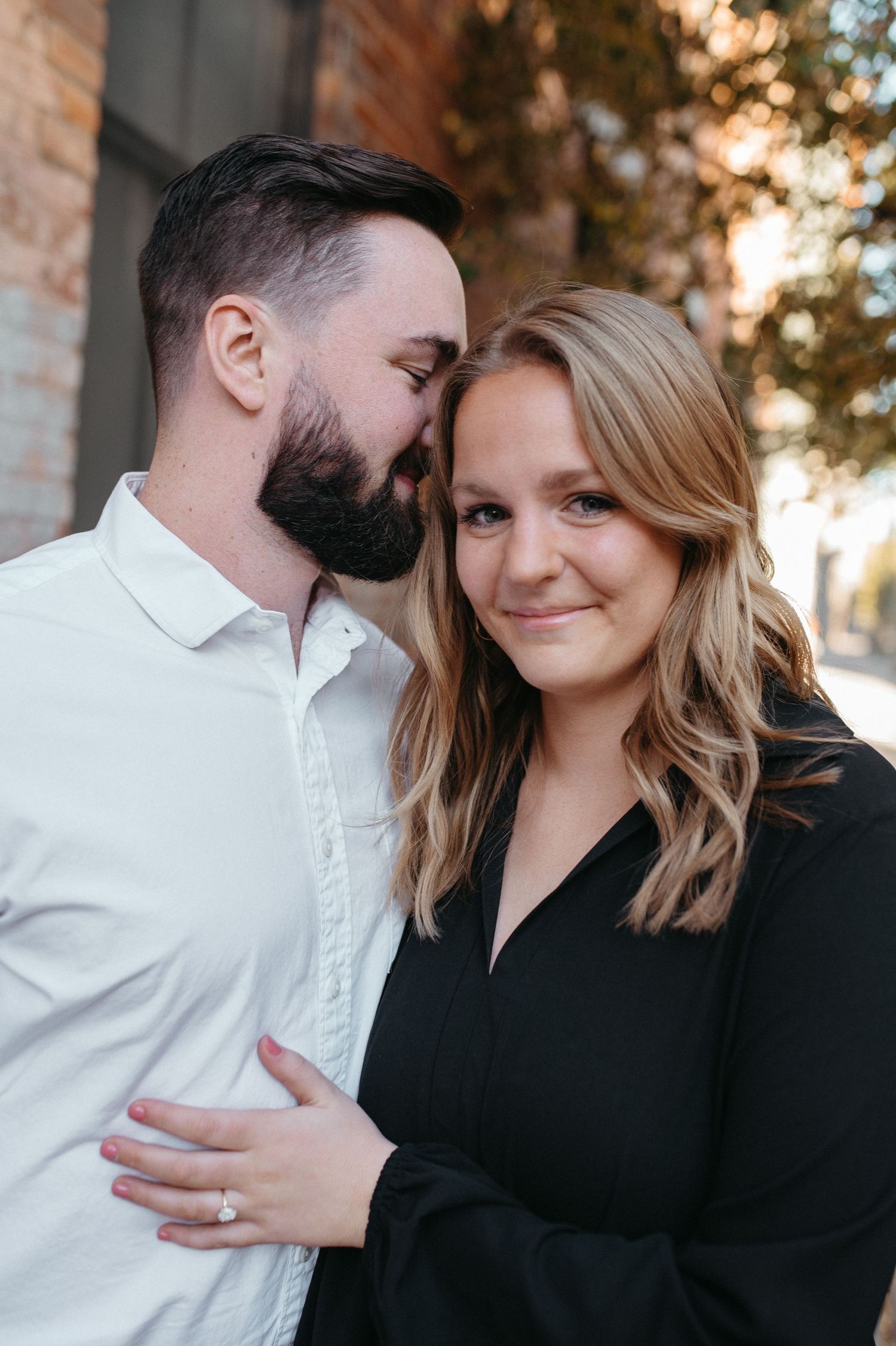 A close-up portrait of a couple in contrasting black and white outfits against a brick wall background.