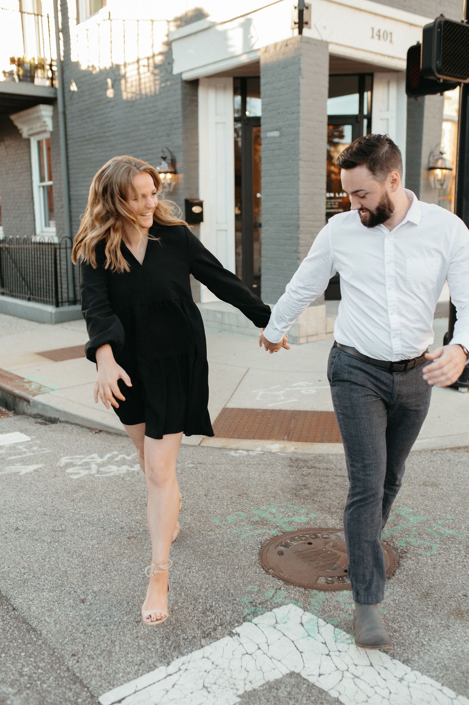 A couple dances playfully on a city street corner wearing formal attire.