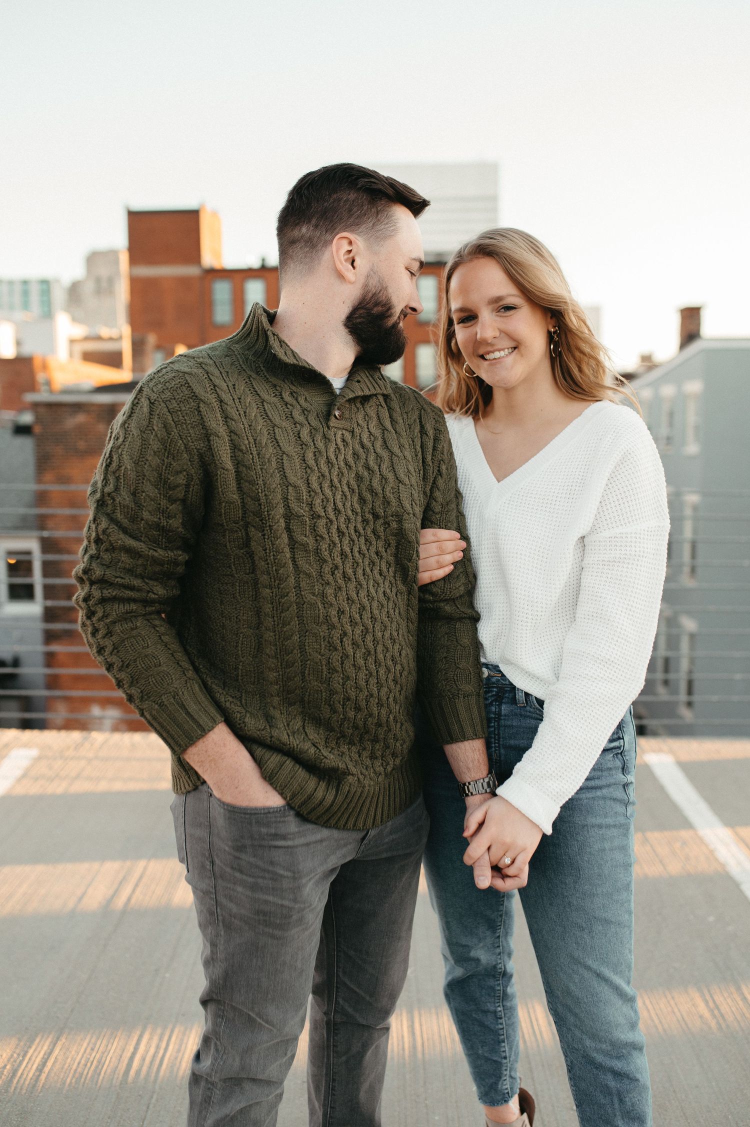 A sweet candid moment between a couple wearing coordinated sweaters on an urban rooftop.