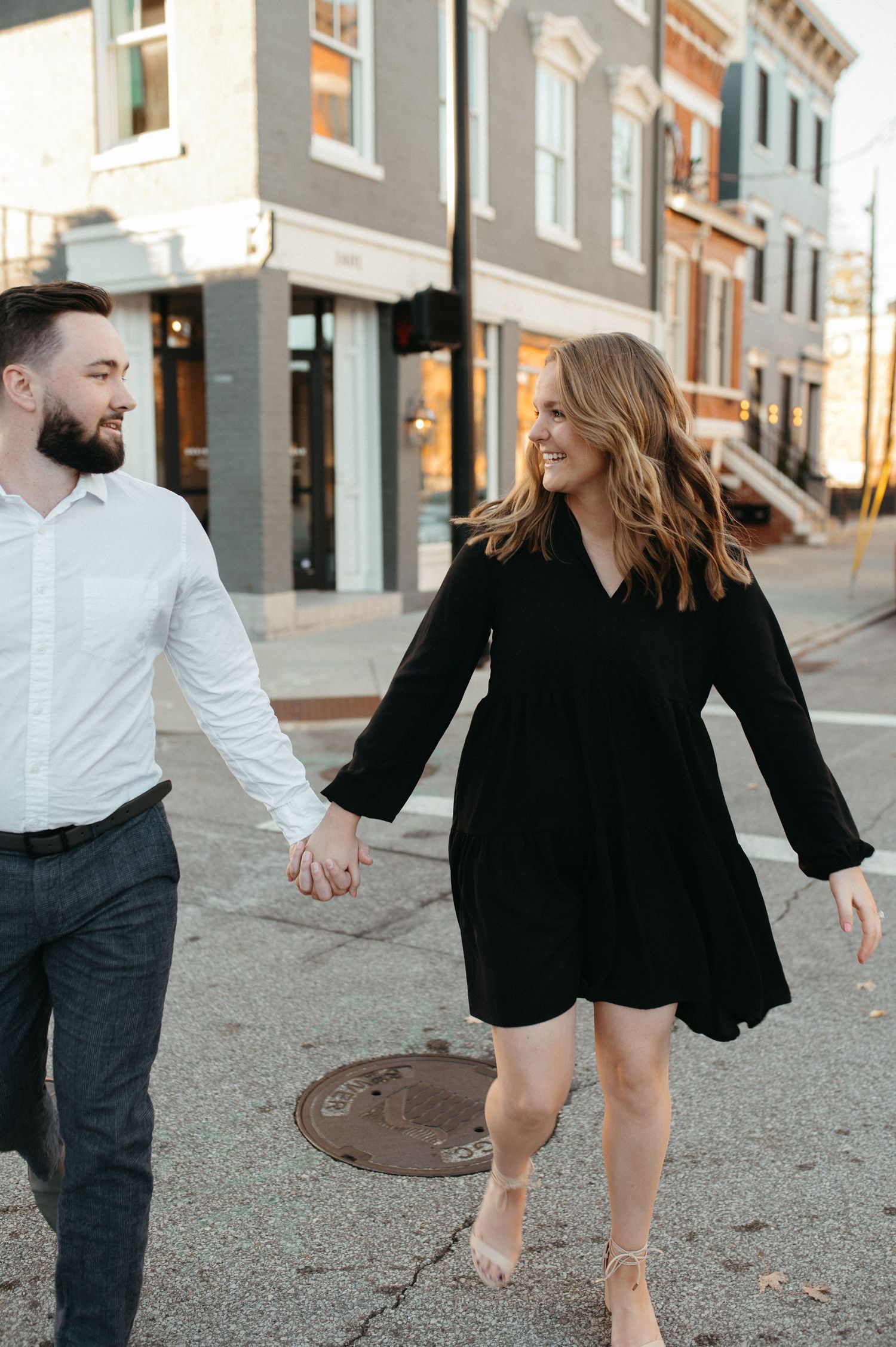 Couple holding hands while walking along a city street with historic buildings in the background.