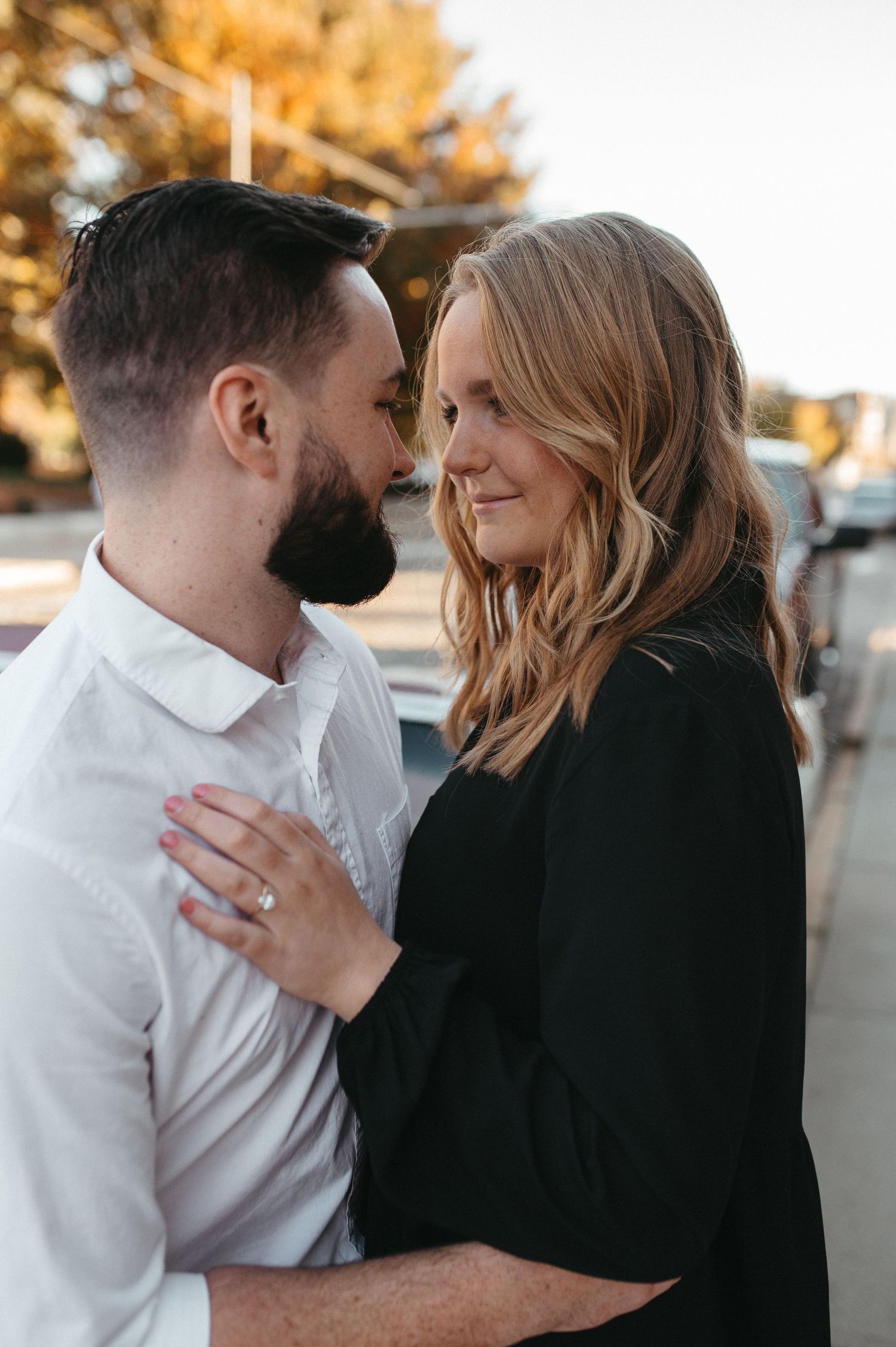 Couple shares a romantic moment showing off an engagement ring beside a classic car.