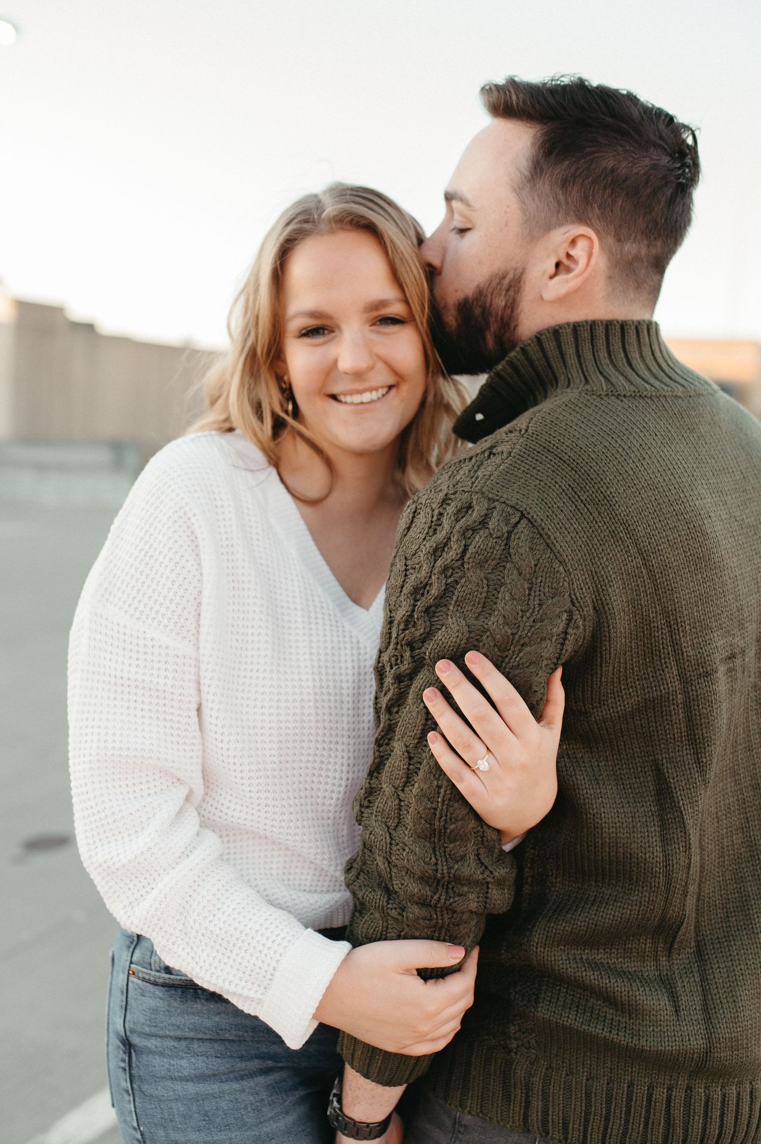 Couple in matching sweaters sharing an affectionate moment on a city rooftop.