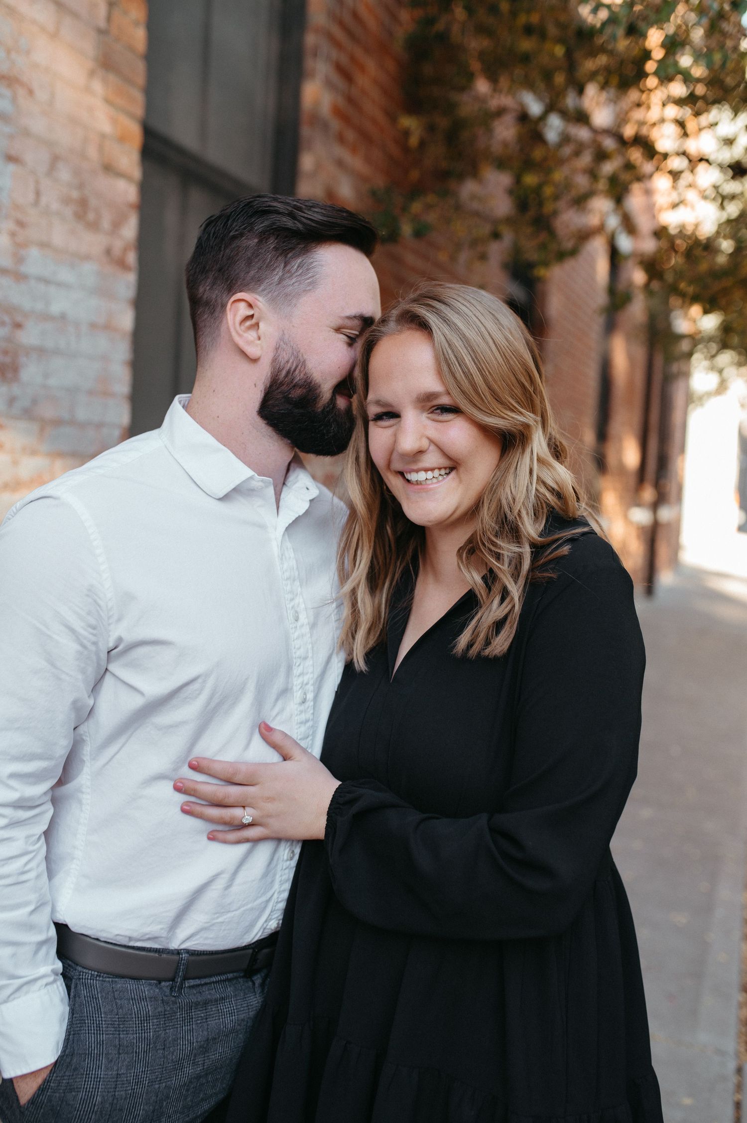 A tender moment captured between a couple in coordinated outfits against a brick building exterior.