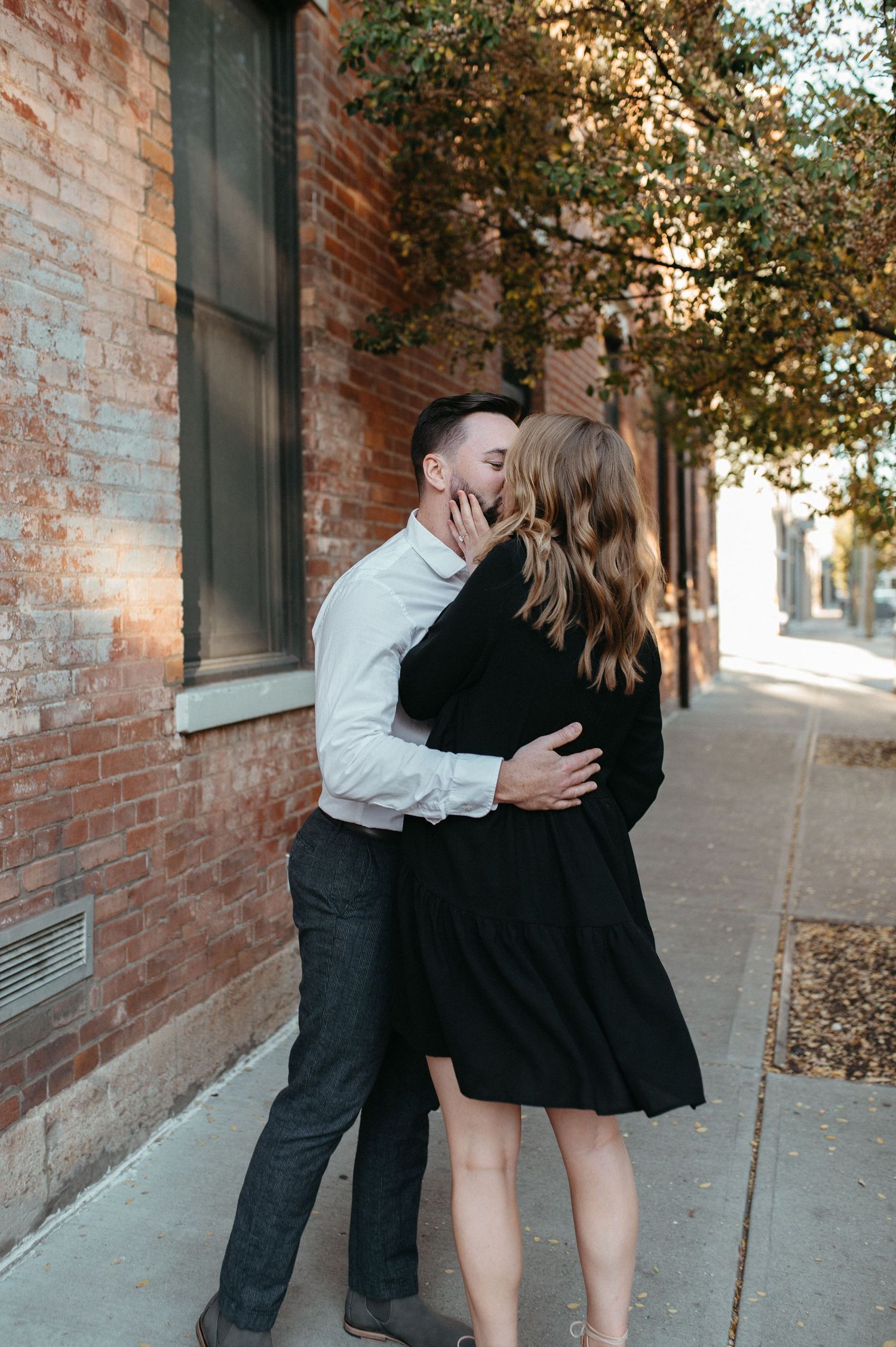 Couple sharing an intimate moment against a rustic brick wall background on an autumn day.