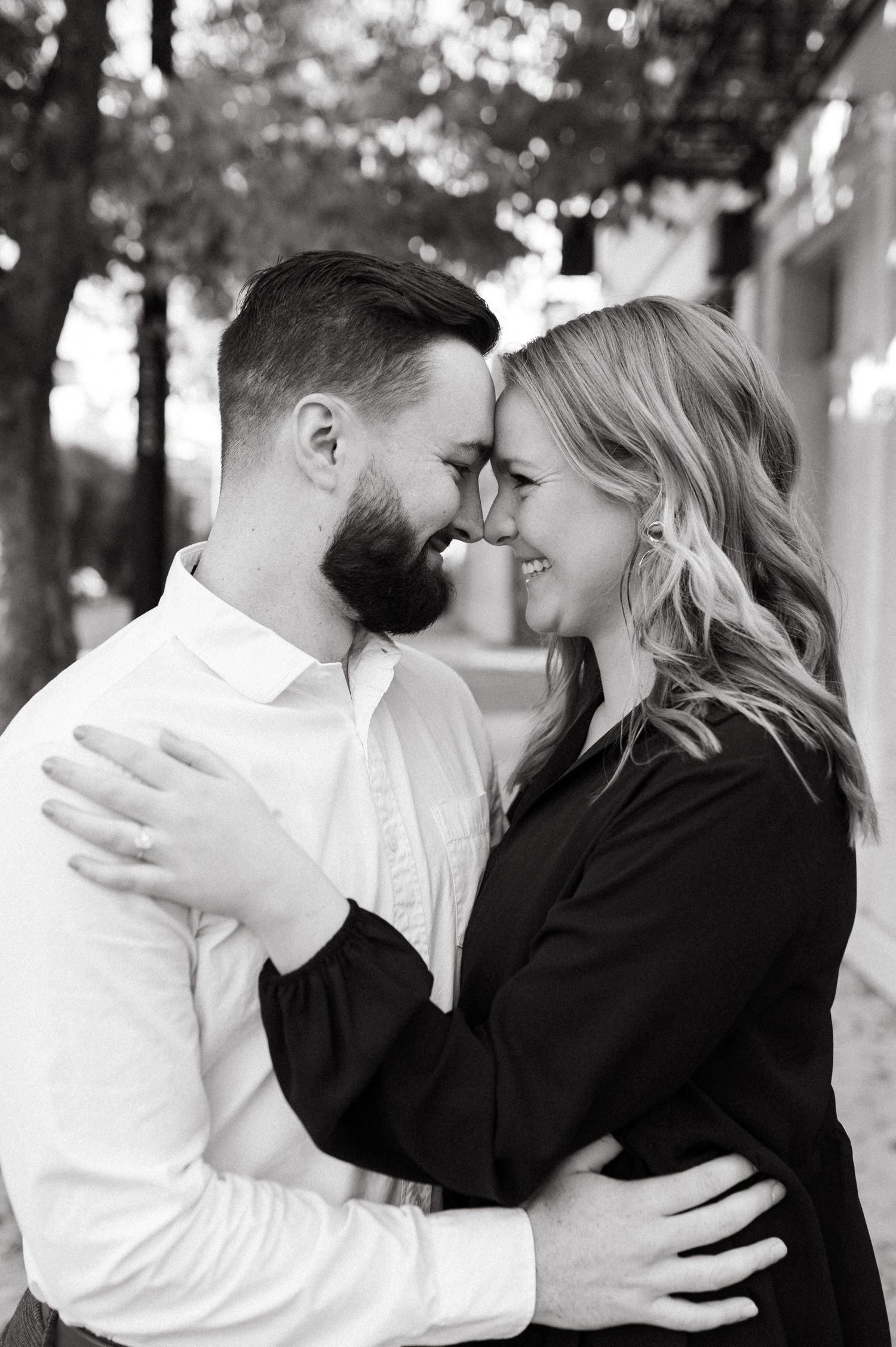 Couple sharing an intimate moment on a street with fall foliage and urban architecture.
