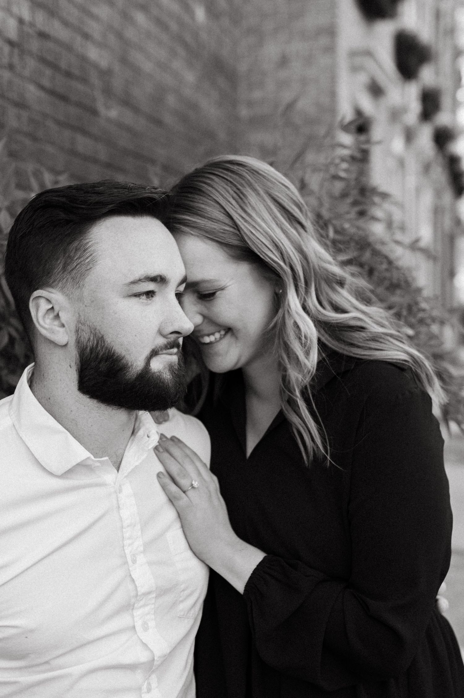 Black and white portrait of a couple sharing an intimate moment against a brick wall.