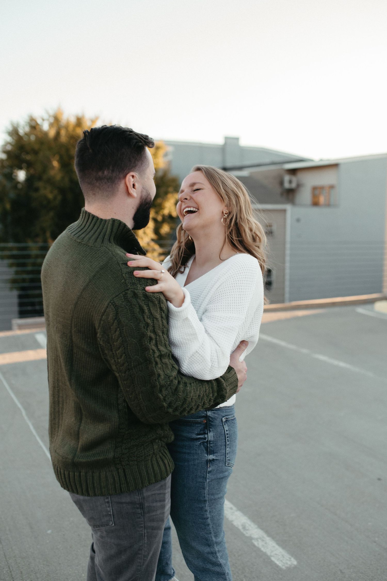 A joyful couple laughing together on a rooftop parking area at sunset.