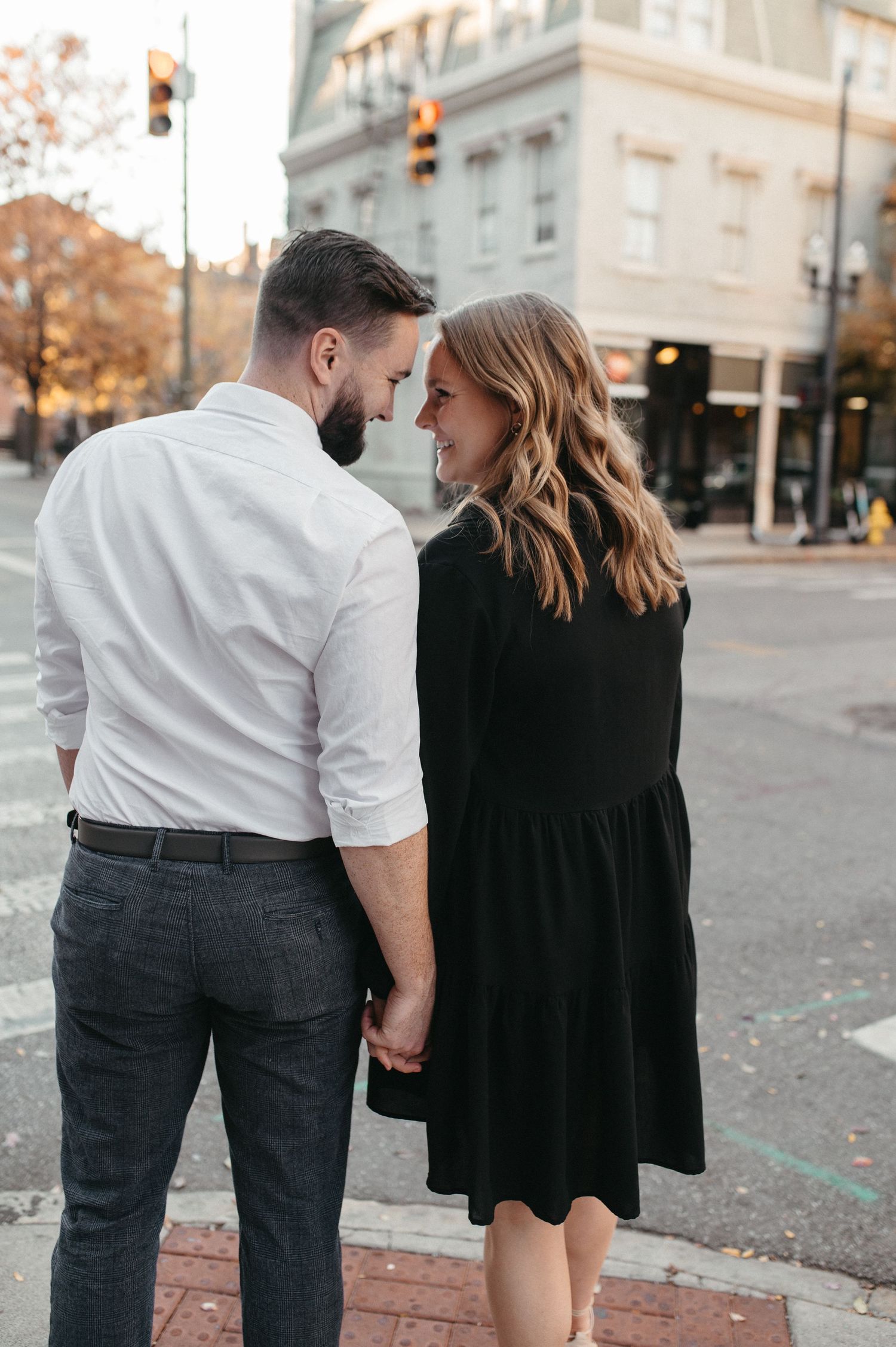 A romantic couple shares an intimate moment on a city street corner during autumn.
