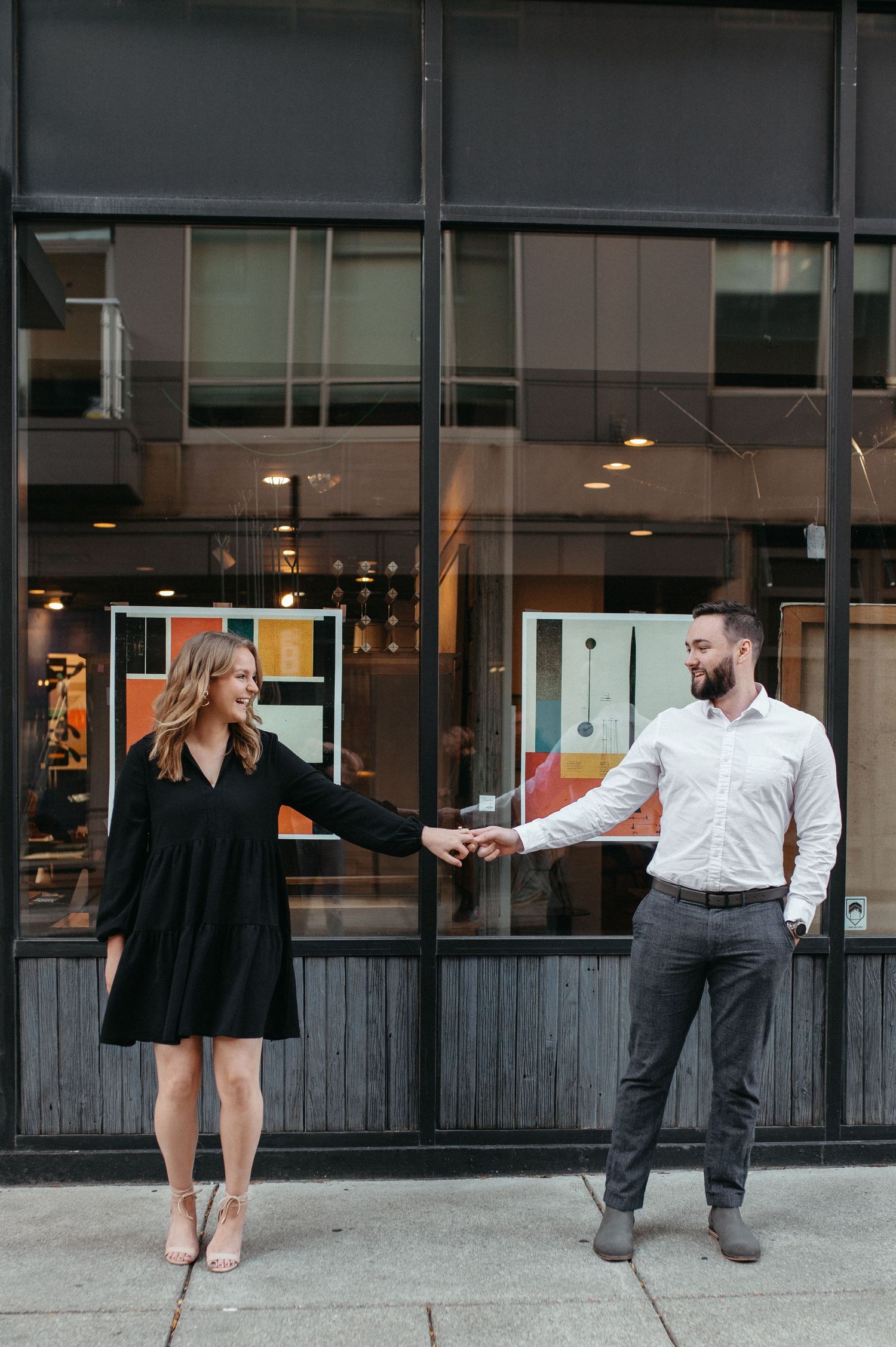 Couple dancing playfully outside a modern storefront in the city.