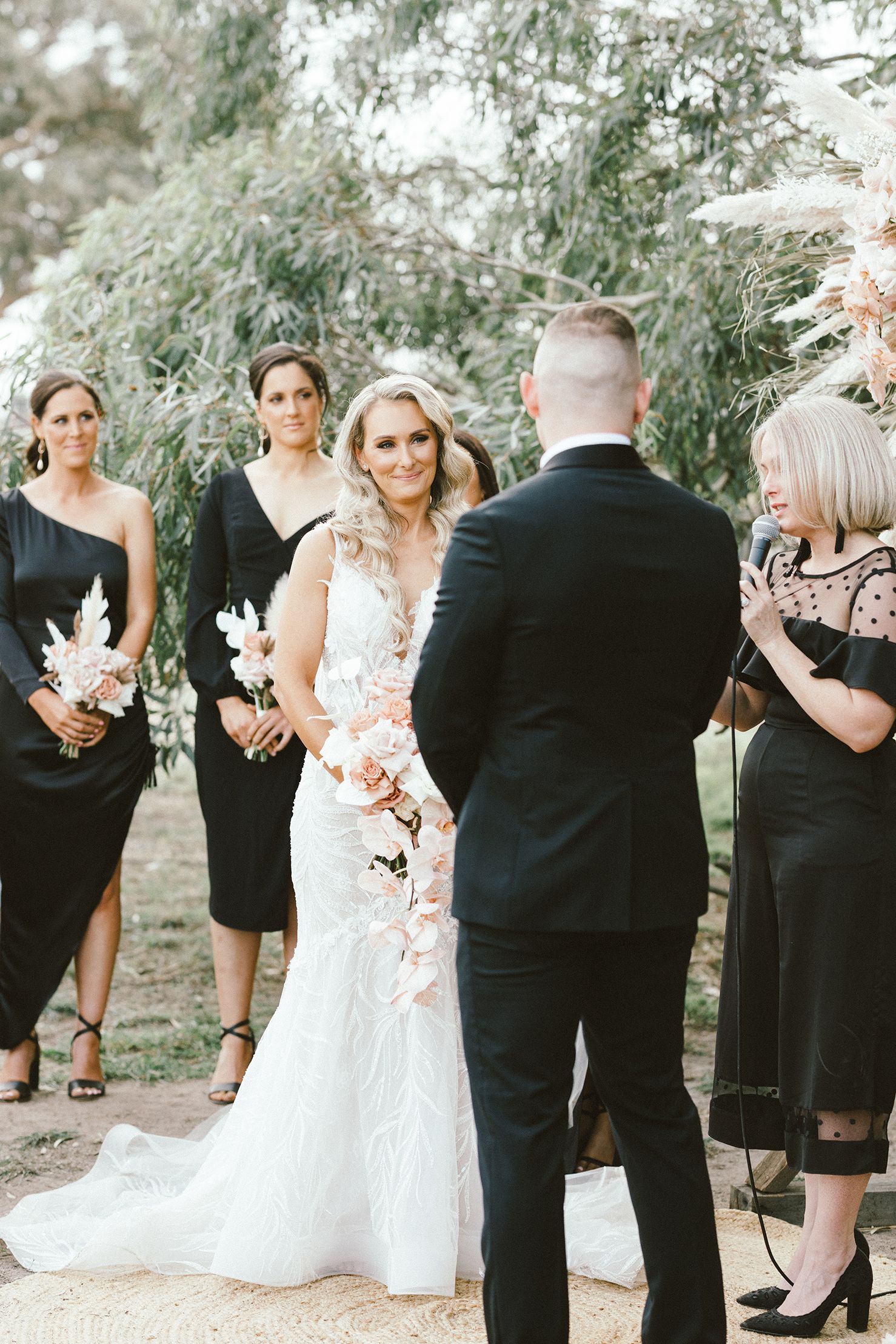 Wedding party in black and white attire stands during outdoor ceremony.