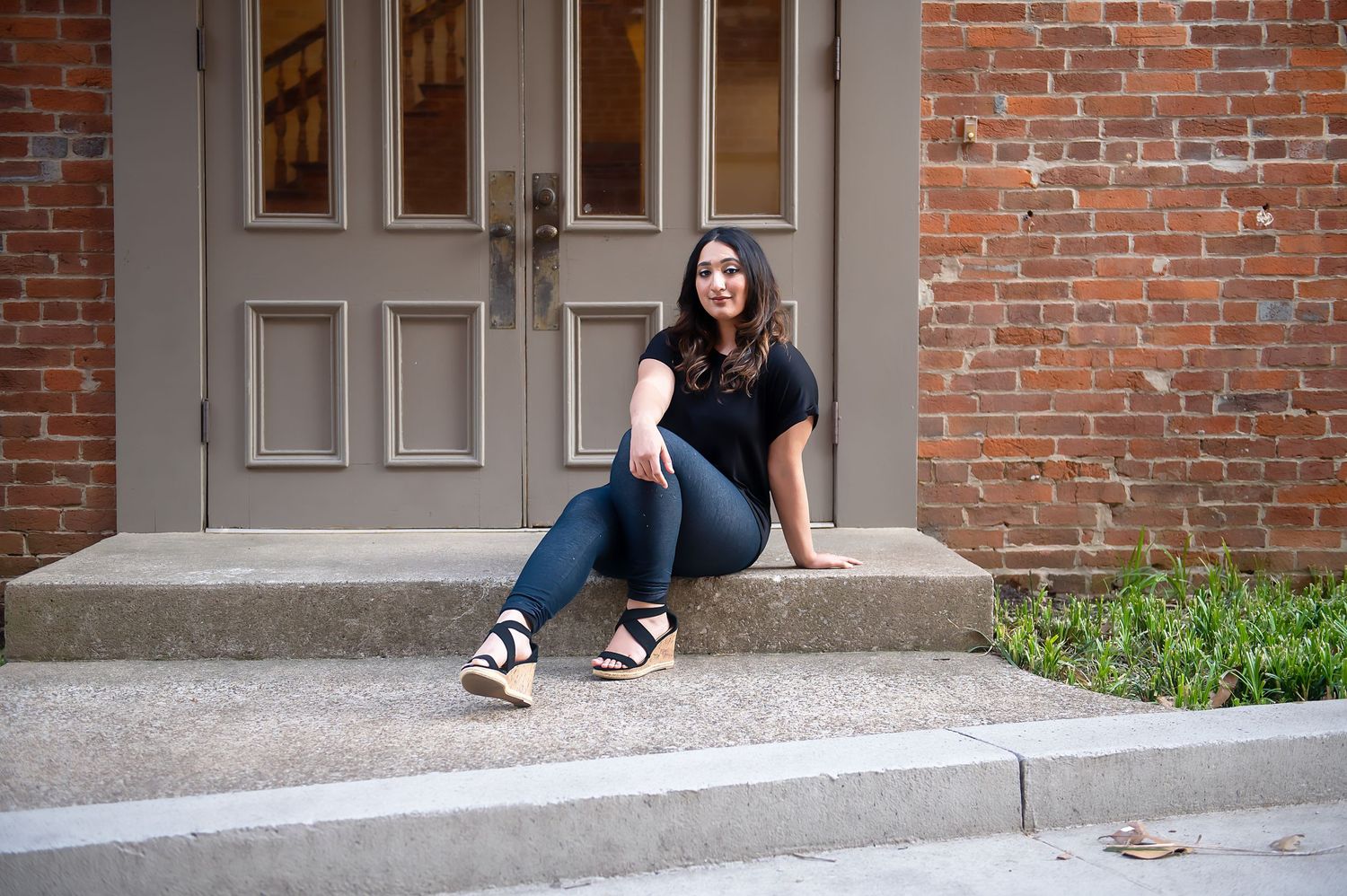 Person in casual attire sitting on concrete steps against brick wall.