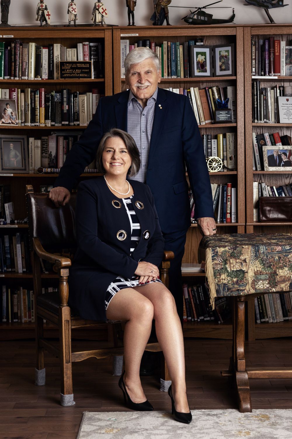 Professional portrait in a home library with bookshelves and military memorabilia.