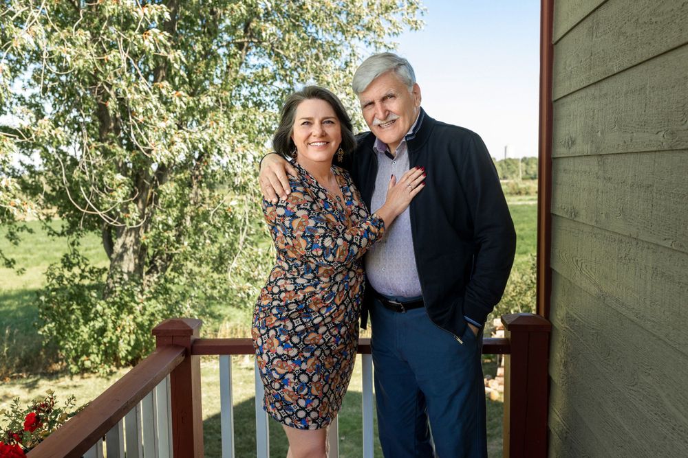 Outdoor portrait of two people on wooden deck with rustic house exterior.