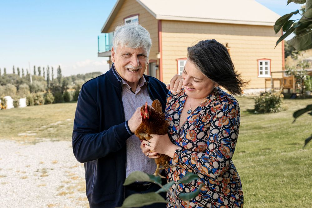A couple shares a joyful moment outdoors while holding a small brown chicken on their rural property.