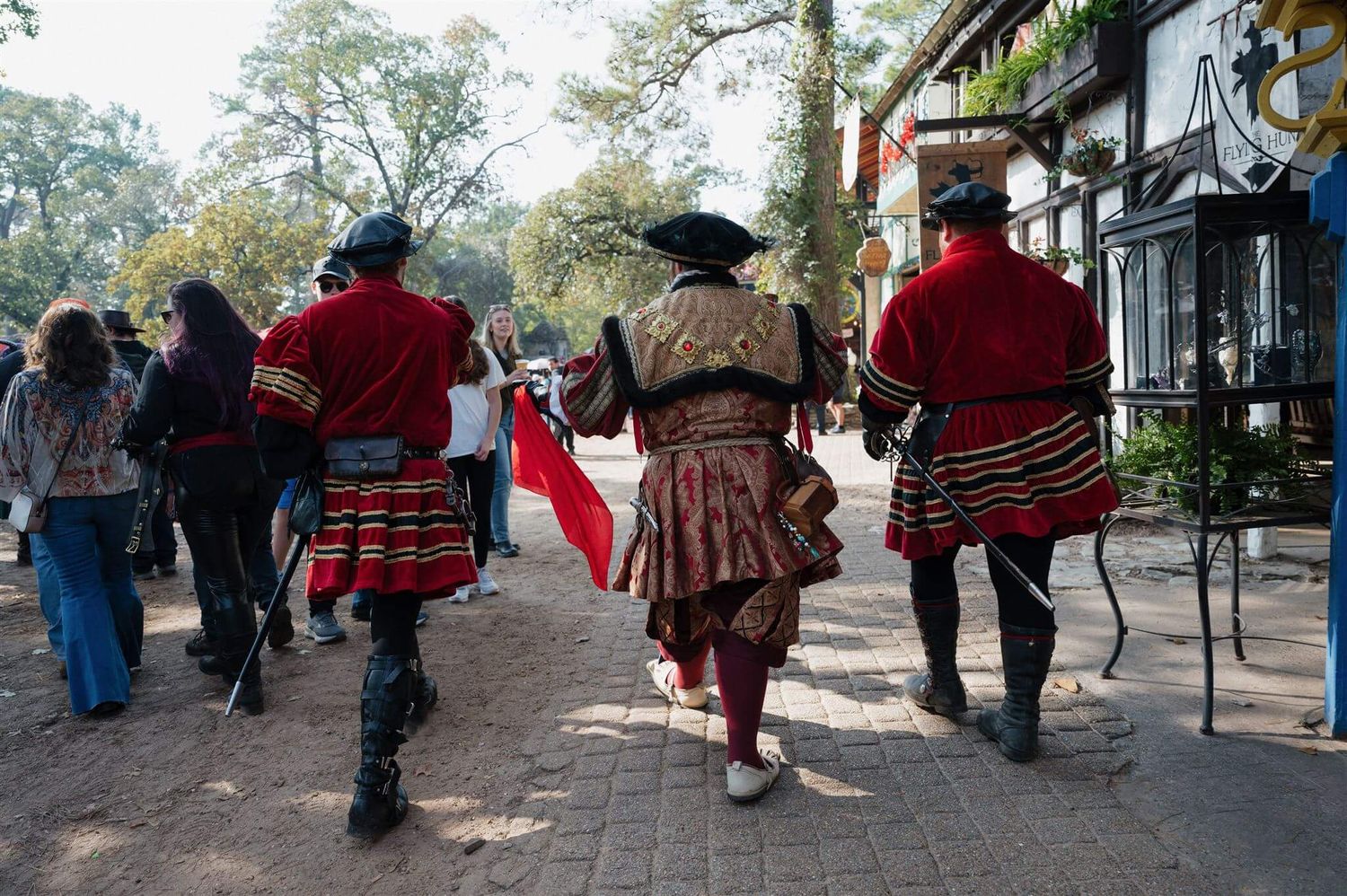Performers in red Tudor costumes walk along a pathway at a Renaissance festival.
