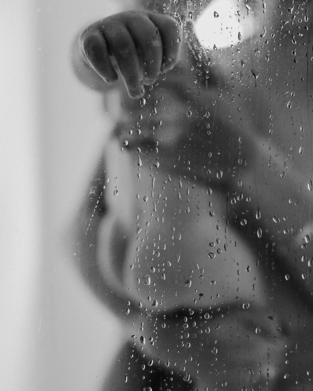 Black and white silhouette of pregnant woman behind wet glass shower door.