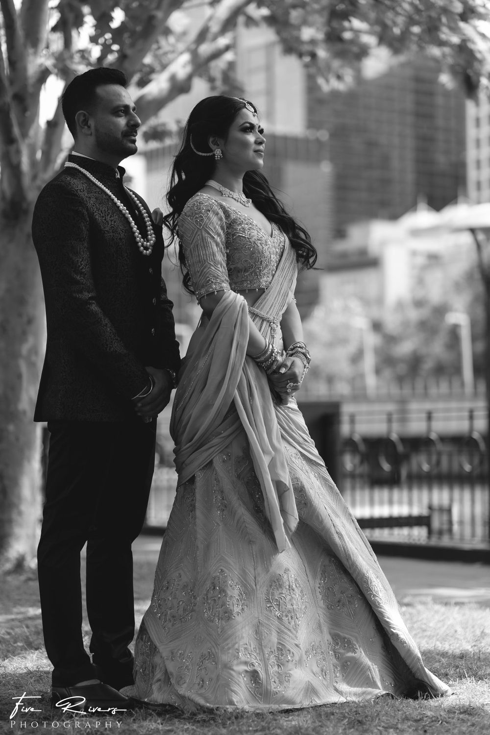 An elegant black and white portrait of a couple in wedding attire standing in a garden setting.