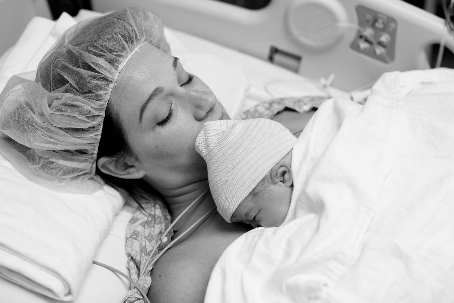 Black and white hospital photo capturing tender moment between mother and newborn.