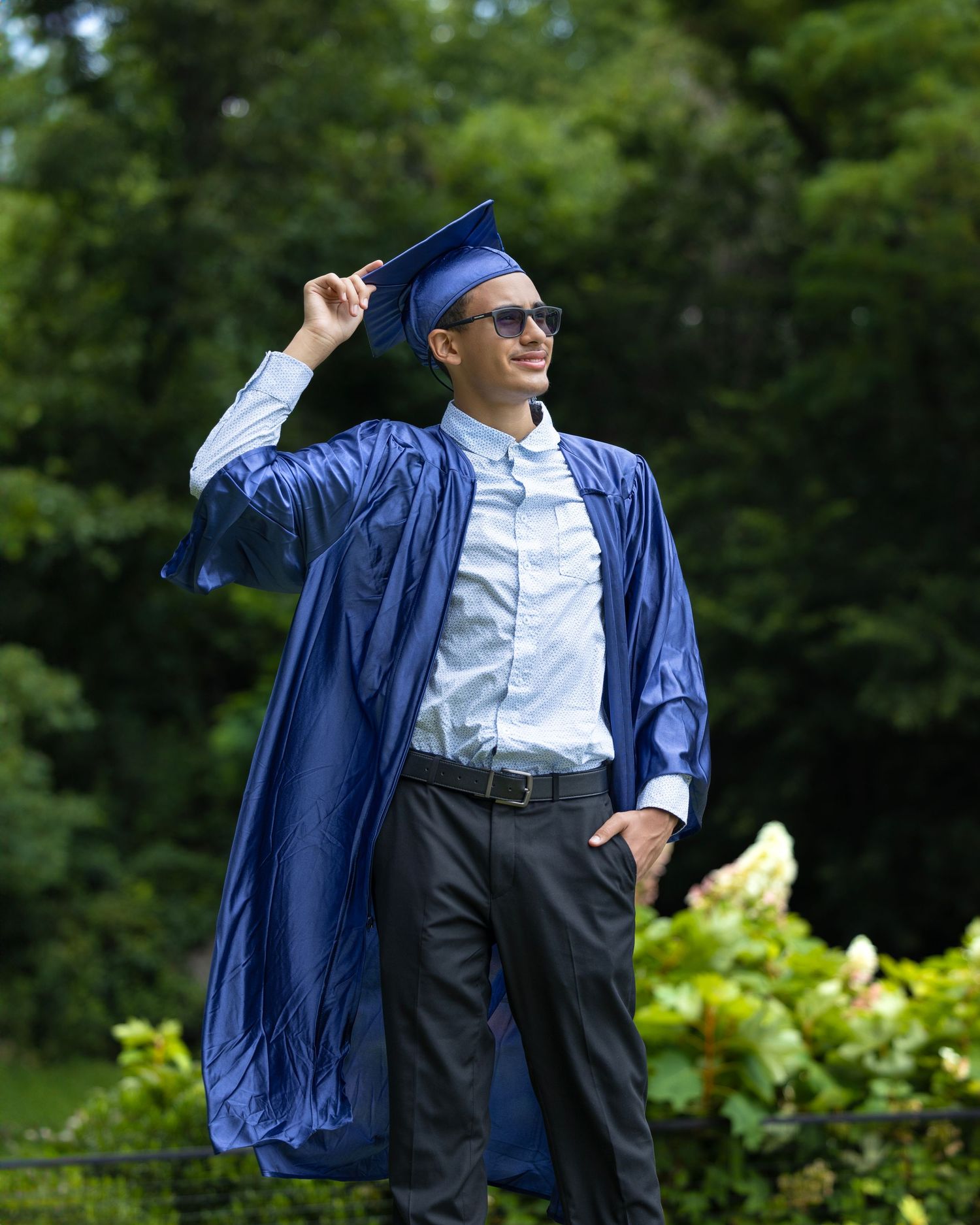 Graduate in blue cap and gown poses joyfully outdoors during commencement ceremony.