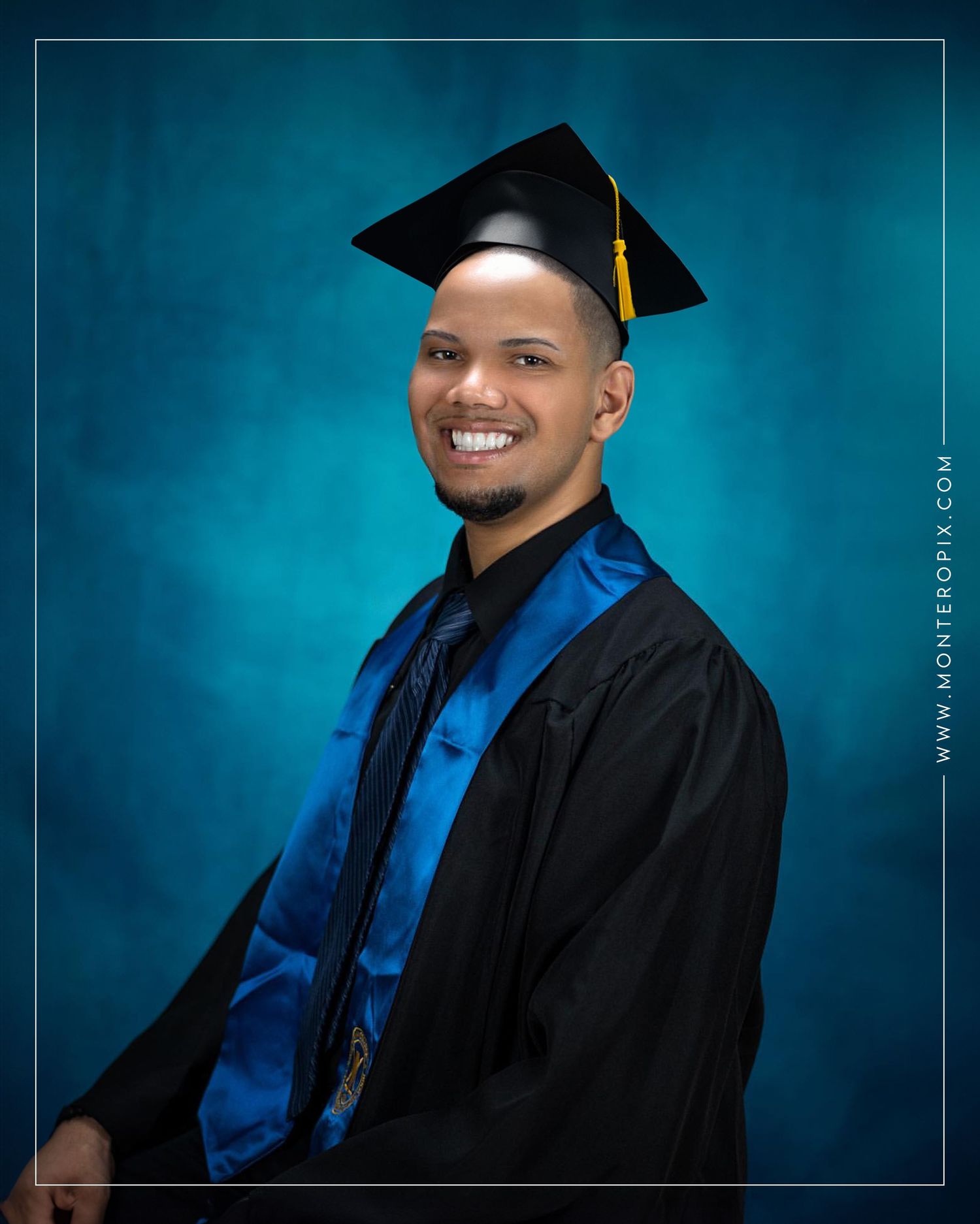 Graduate in black cap and gown with blue stole poses against turquoise backdrop.