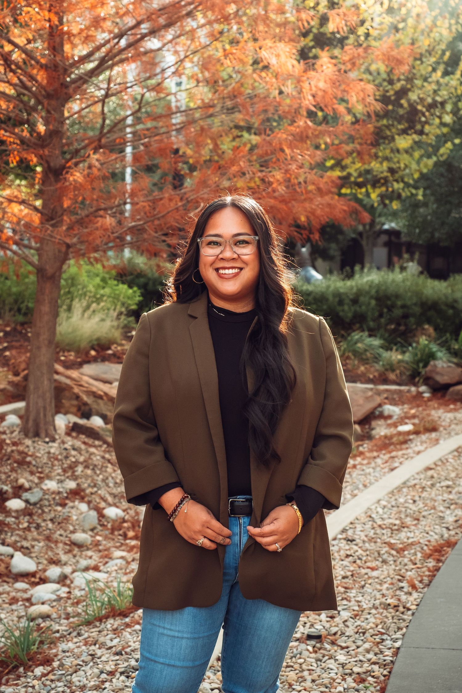 Autumn photoshoot in a park with brown coat and jeans against vibrant orange fall foliage.