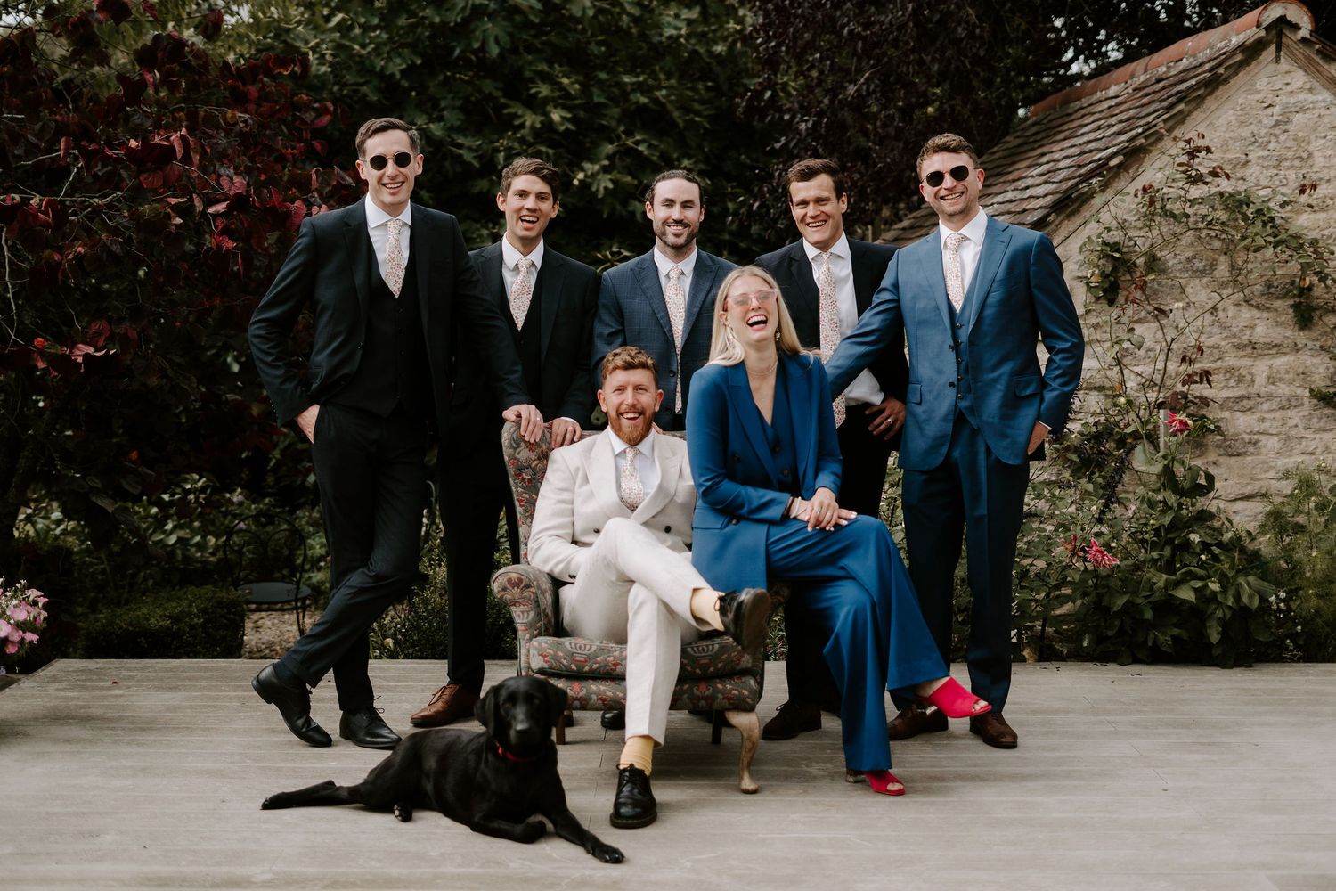 groom sat on chair in garden surrounded by his wedding party and dog before the wedding ceremony in oxfordshire