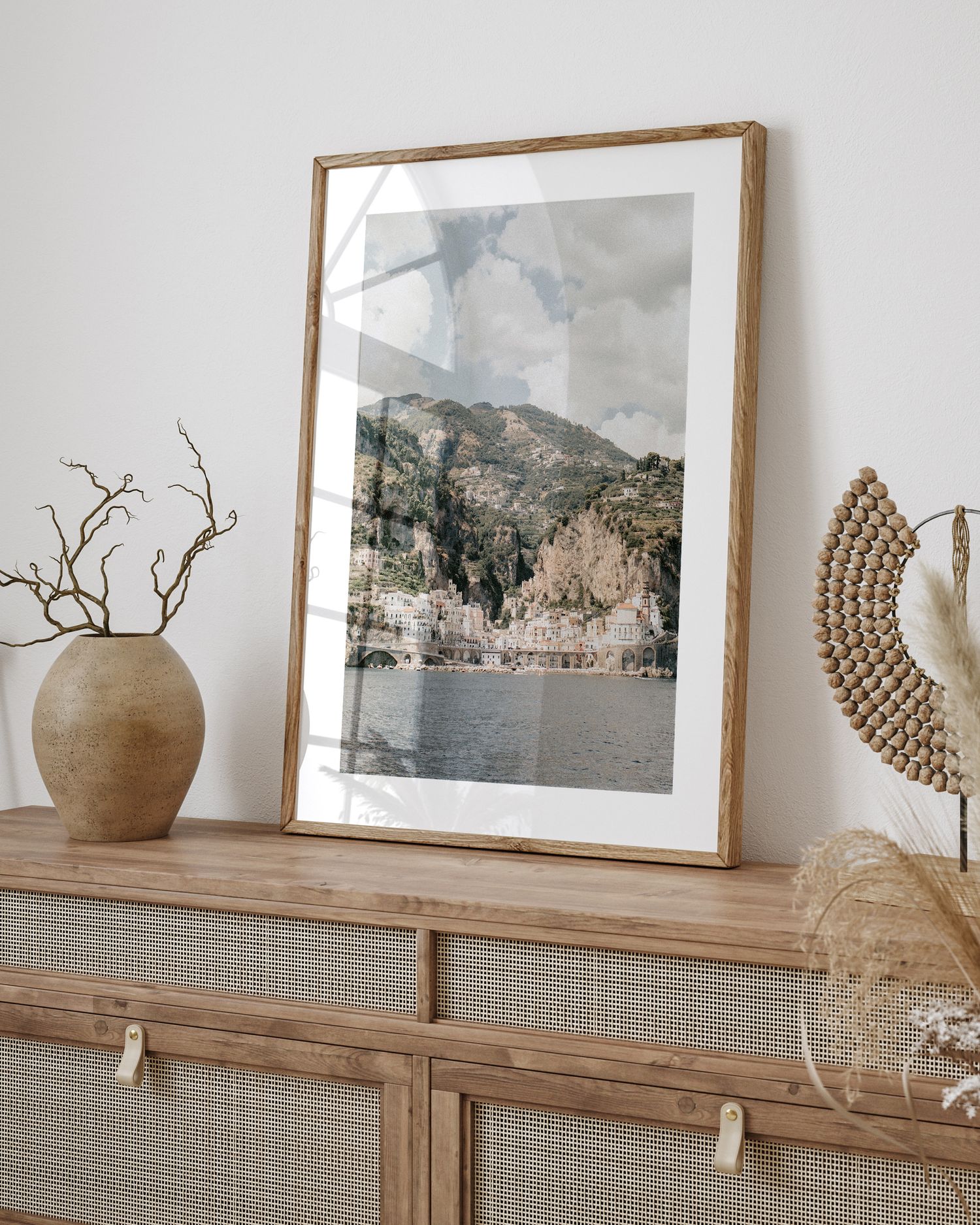 Framed coastal mountain landscape photograph displayed on wooden cabinet with decorative vase.
