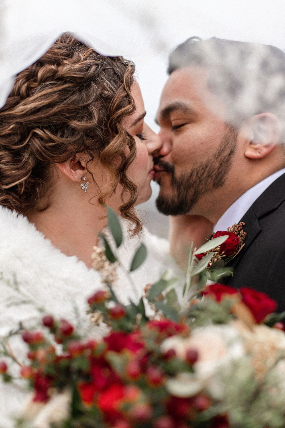 A romantic winter wedding moment with red floral bouquet details.