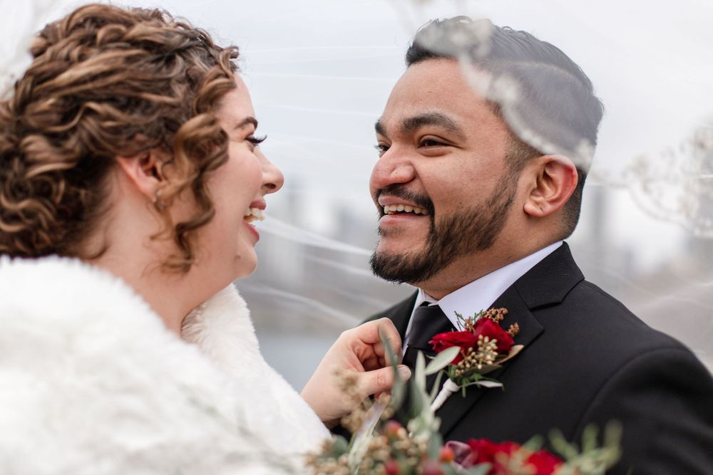 A joyful winter wedding portrait with red boutonniere and white fur wrap details.