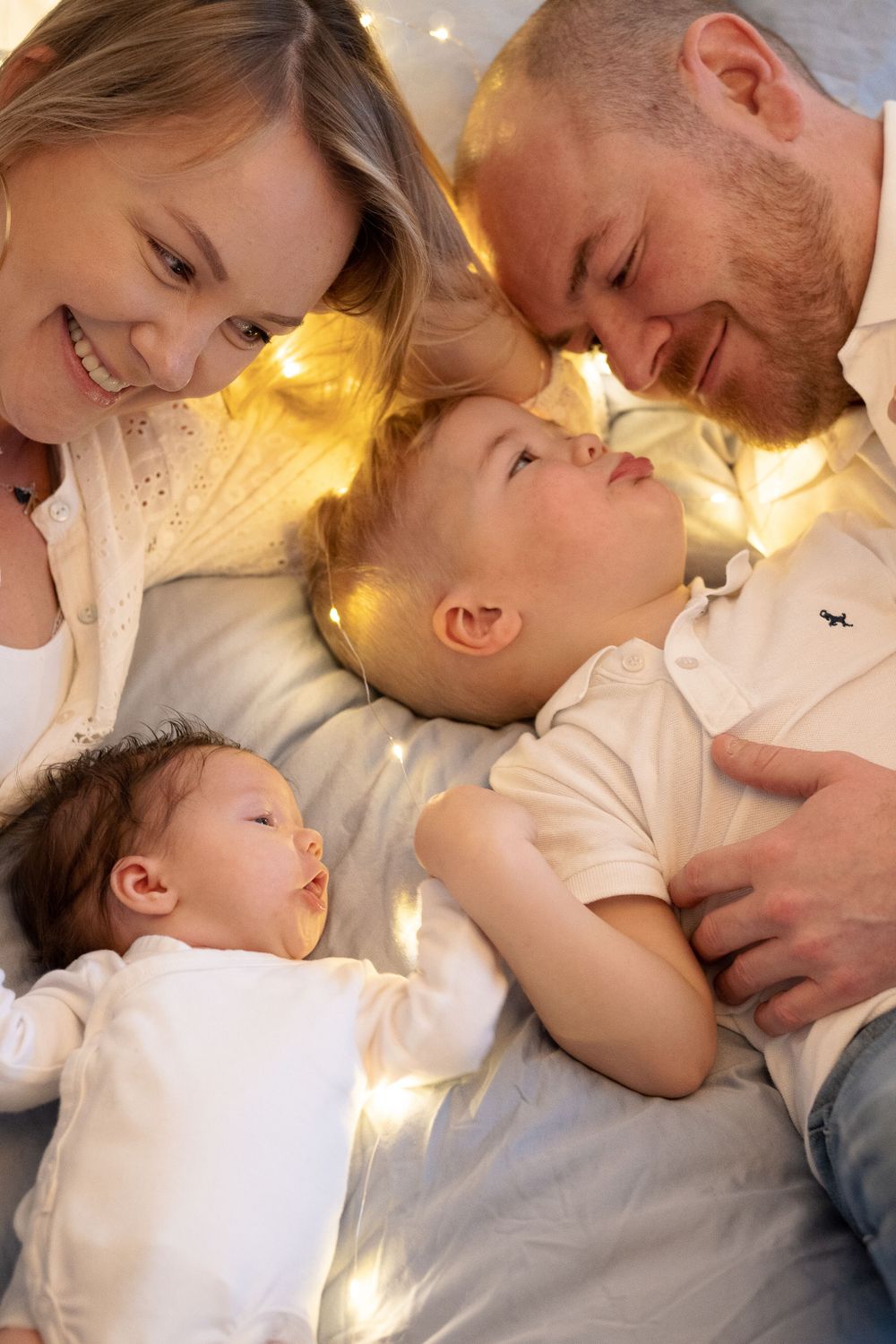 A family is lying on the bed with a little boy and a newborn baby.