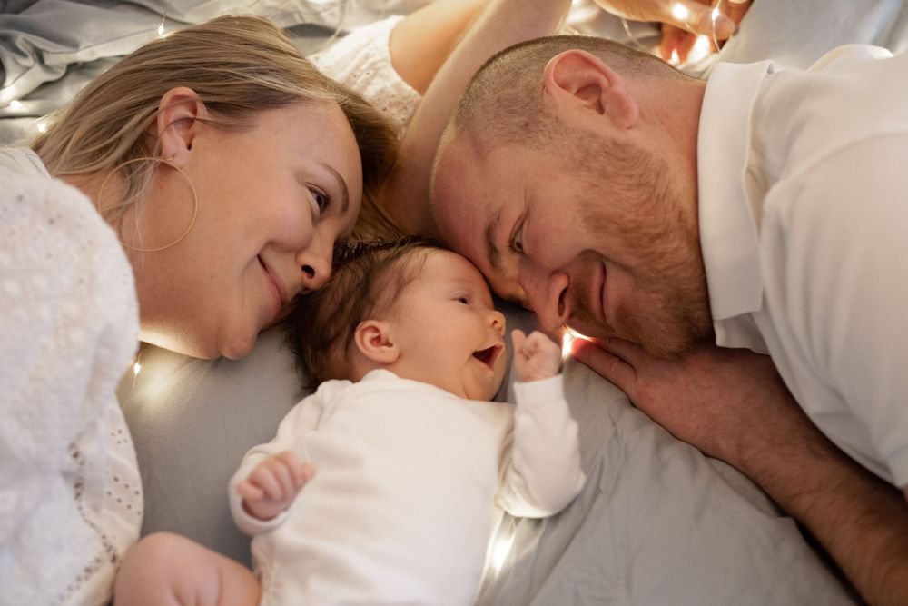 Mother and father are lying on the bed with a newborn baby in between.