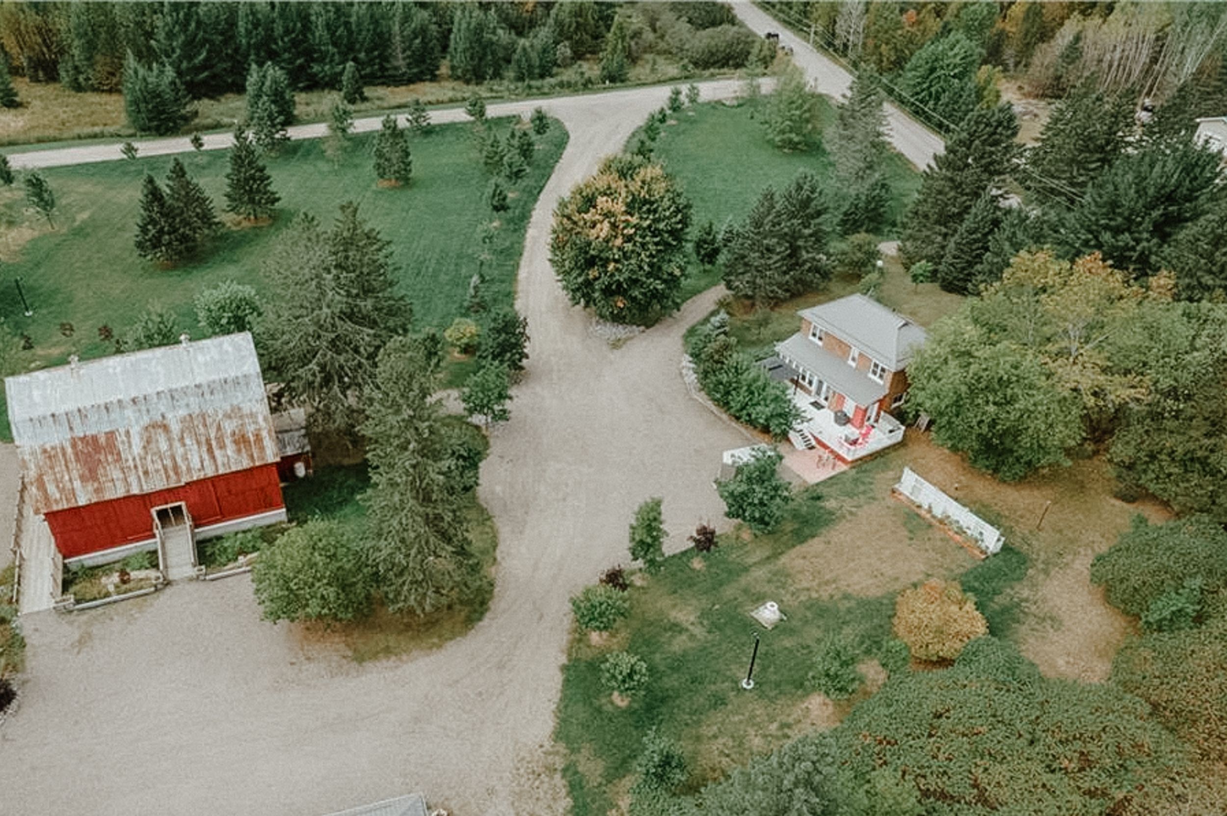 Aerial view of a red barn building and white house surrounded by green trees and winding pathways.