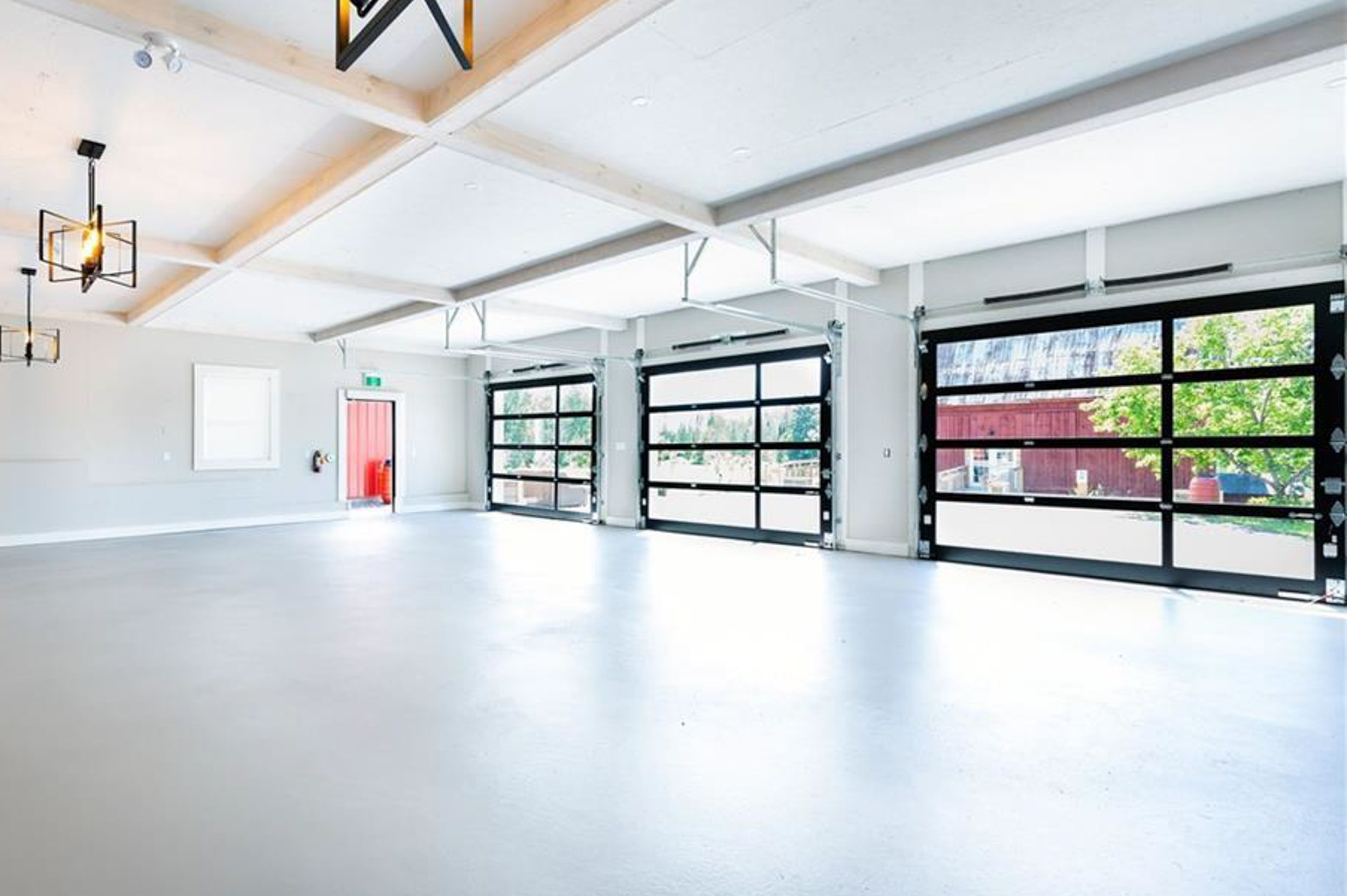 Modern white interior space with large glass garage doors and industrial-style lighting.