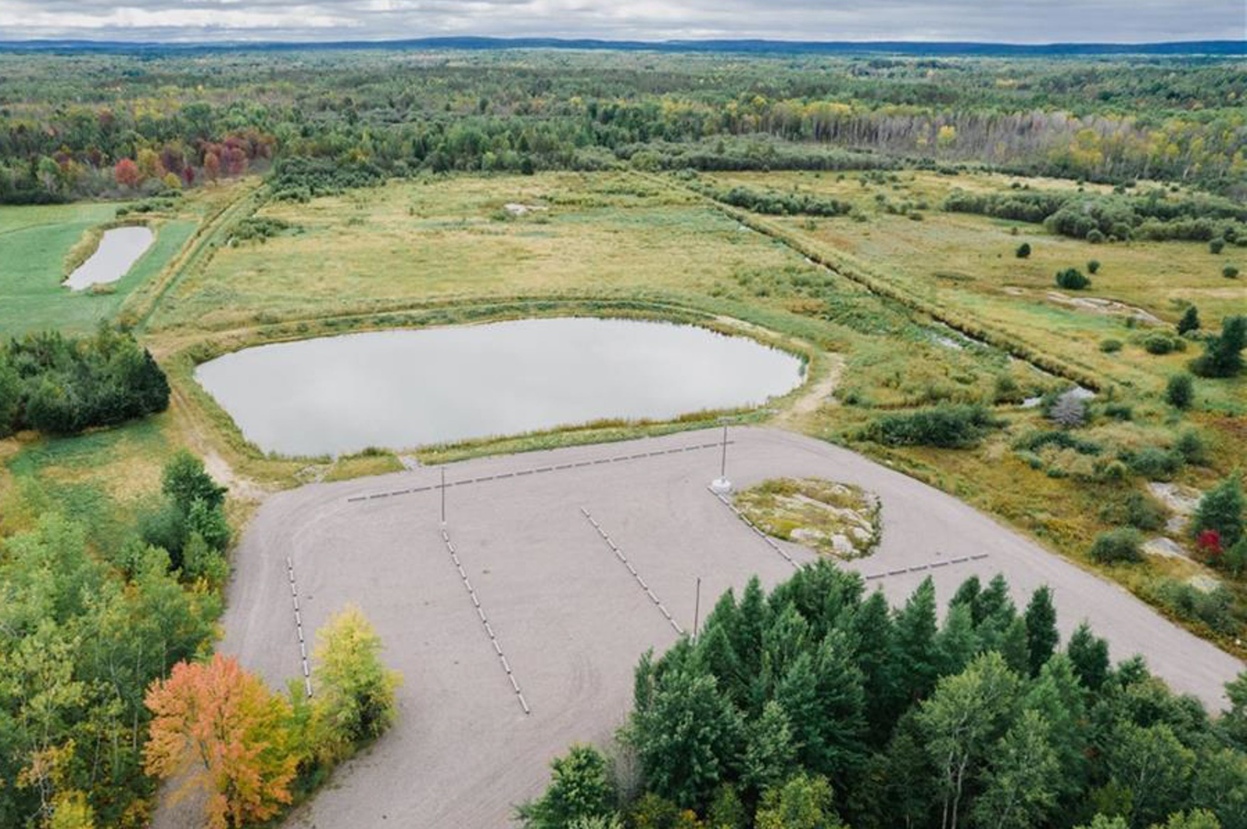 Aerial view of a rural property with a large pond and grassy fields surrounded by forest.