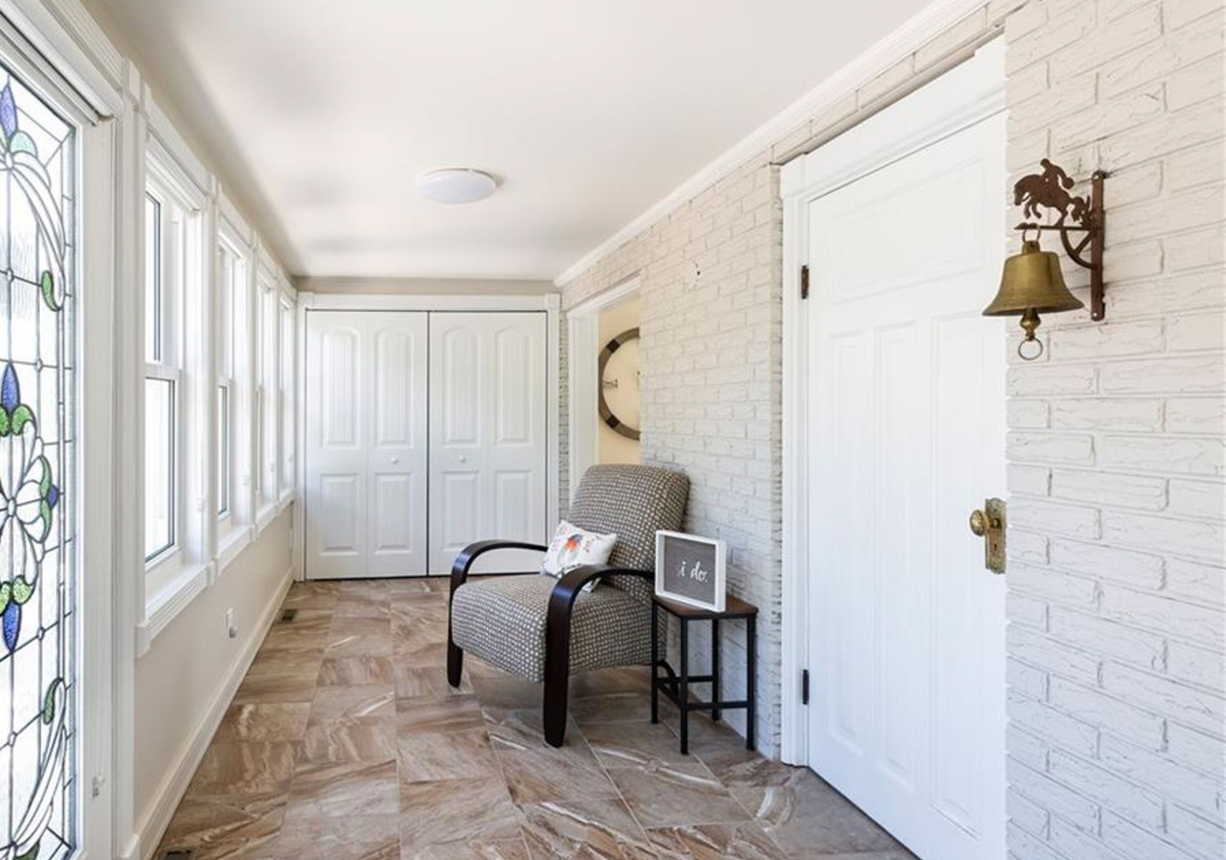 Bright sunlit entryway with white brick walls, decorative windows, and hardwood herringbone flooring.