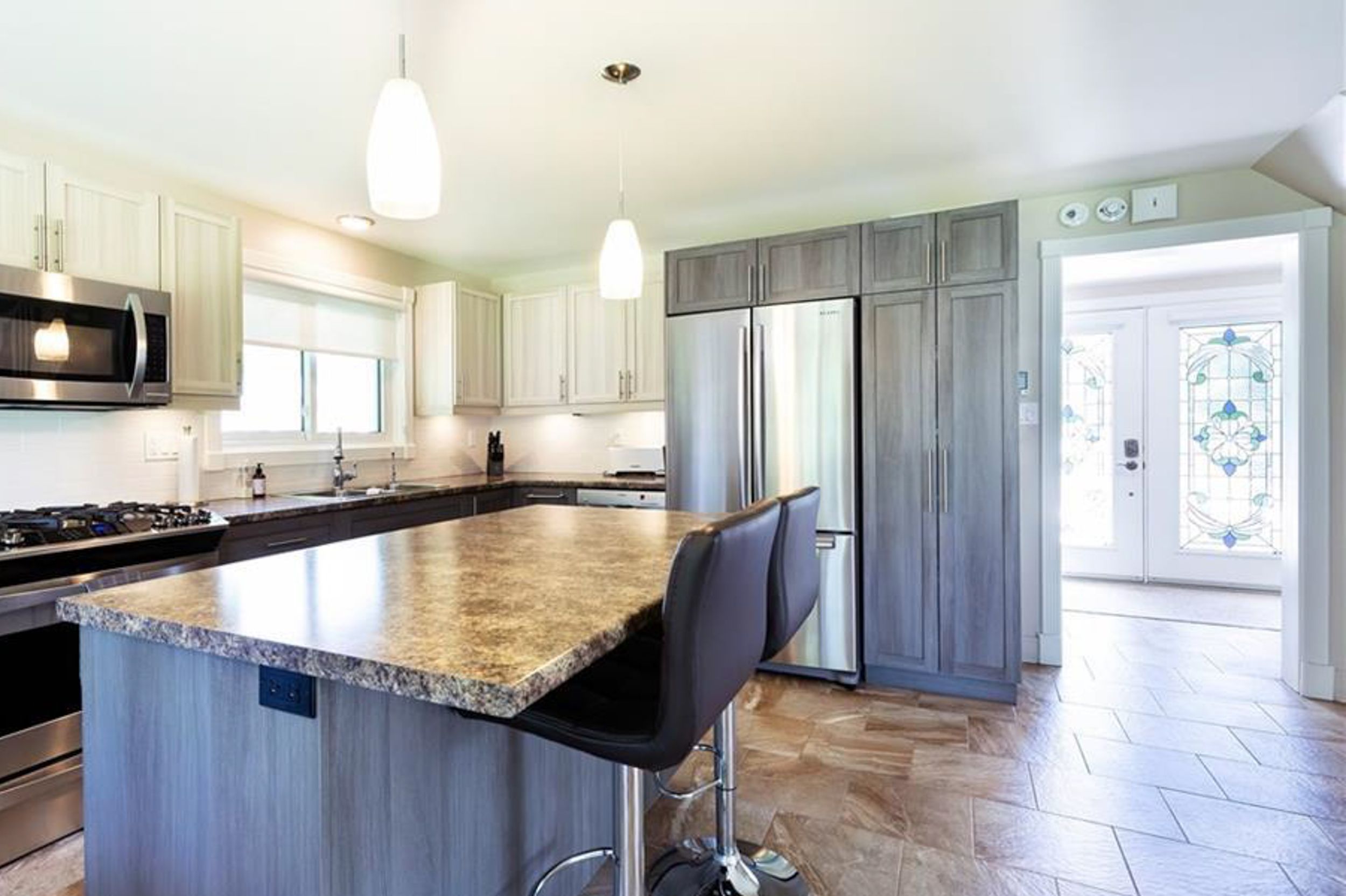Modern kitchen with granite countertops, stainless appliances, and gray cabinetry featuring a large center island.