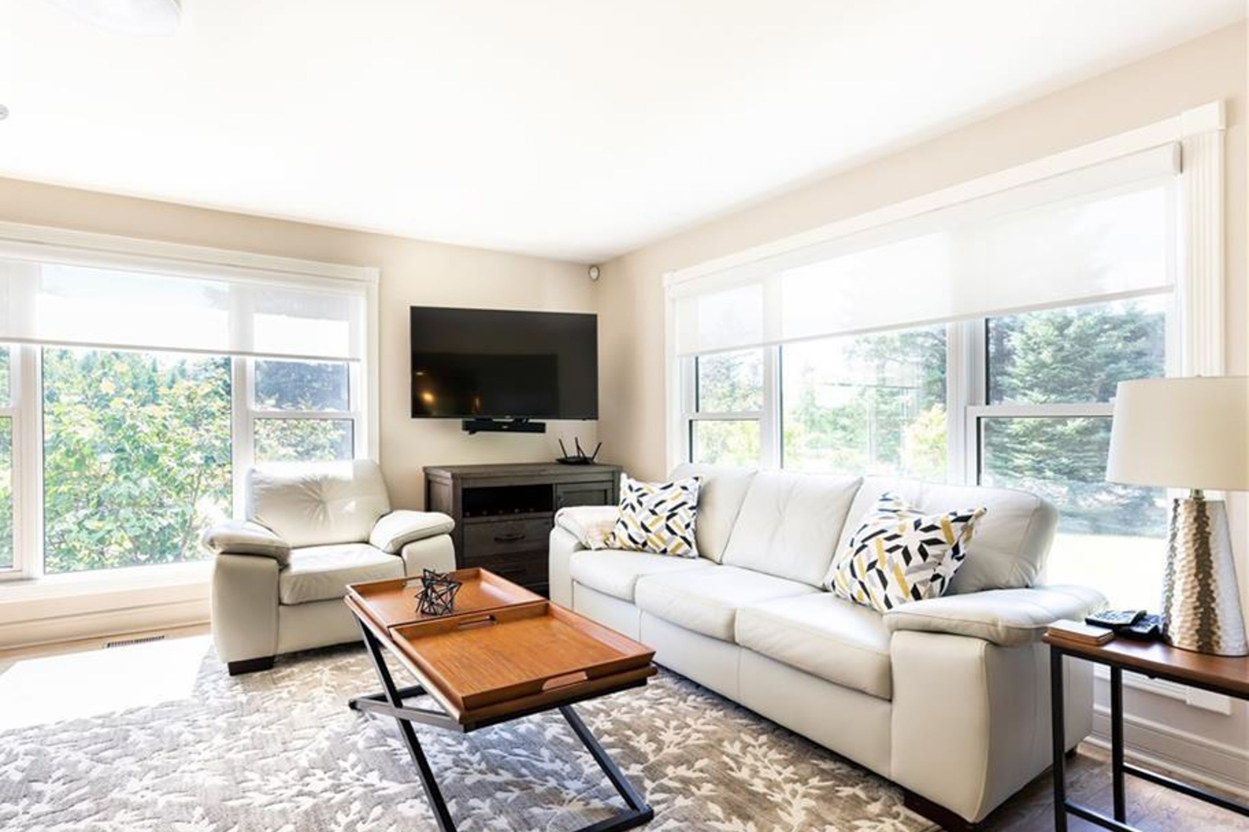 Bright living room with white sofa, wooden coffee table, fireplace and large windows overlooking nature.