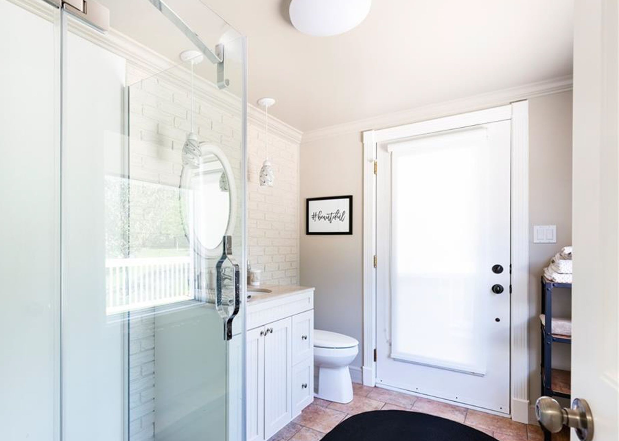 Clean modern bathroom with glass shower enclosure, white vanity, and natural light from window.
