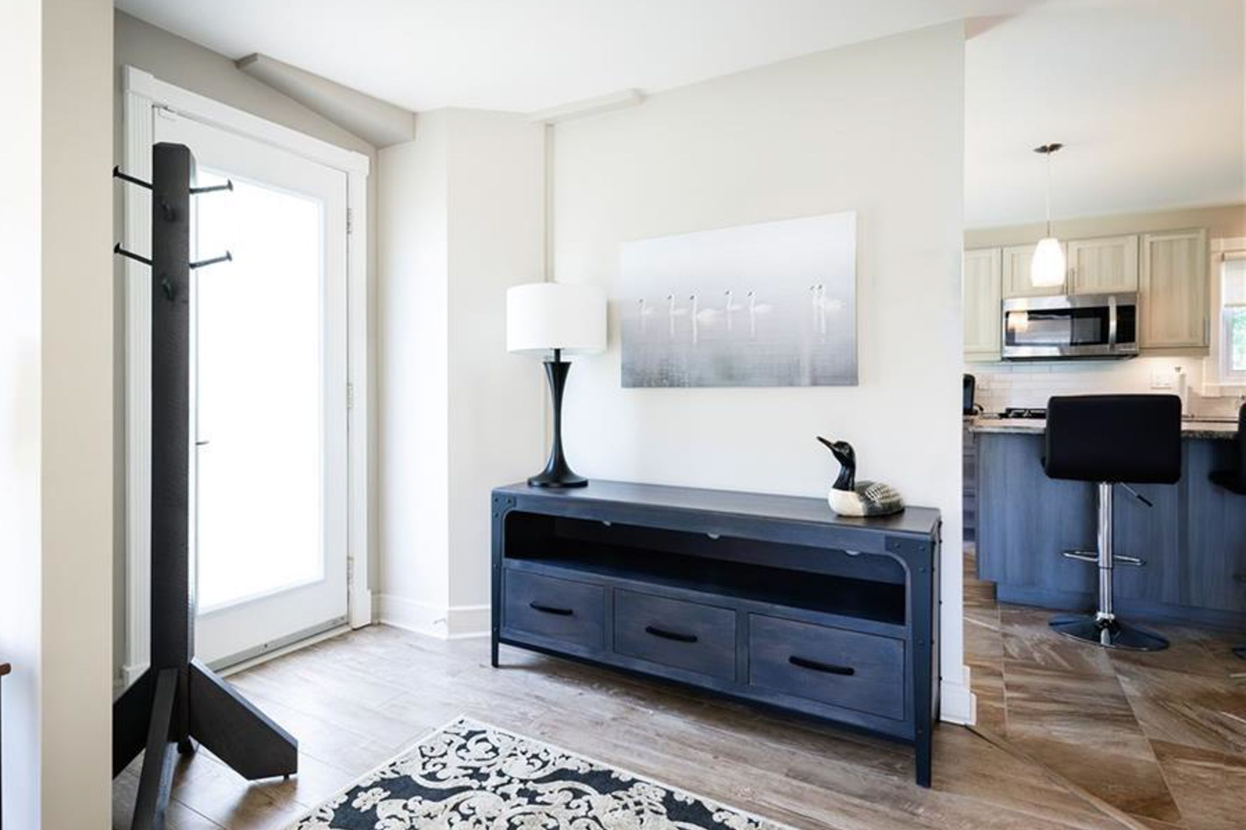 Modern living room features a navy blue console table with lamp and geometric rug against white walls.