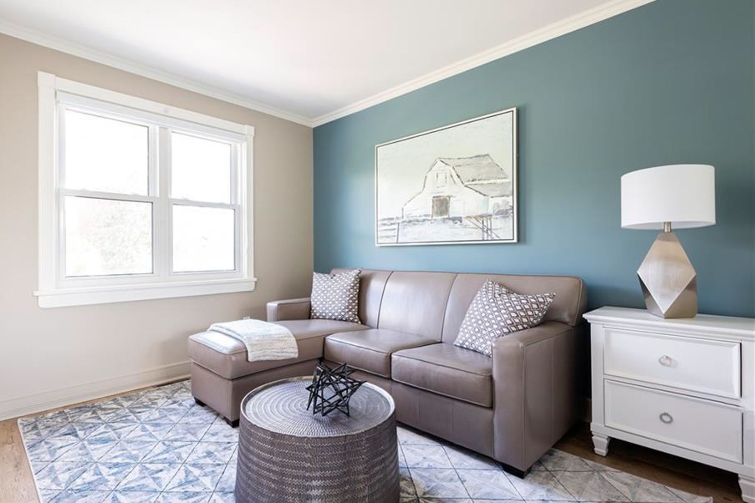 Cozy living area with grey sectional sofa, round coffee table, and coastal artwork on teal accent wall.