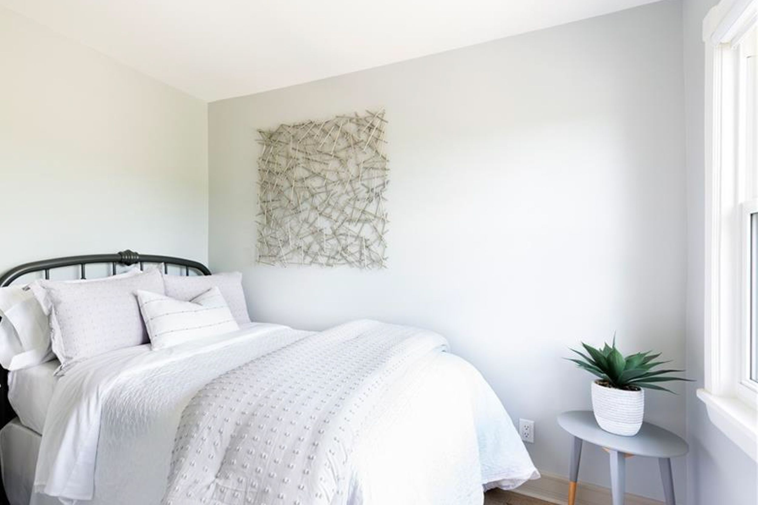 Bright minimalist bedroom with white bedding, black metal headboard, and natural light from window.