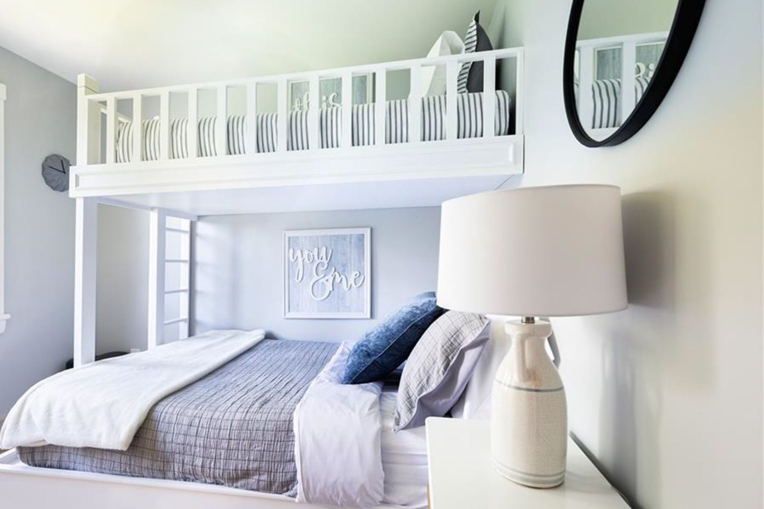Modern bedroom featuring a white loft bed with grey bedding and round mirror accent.