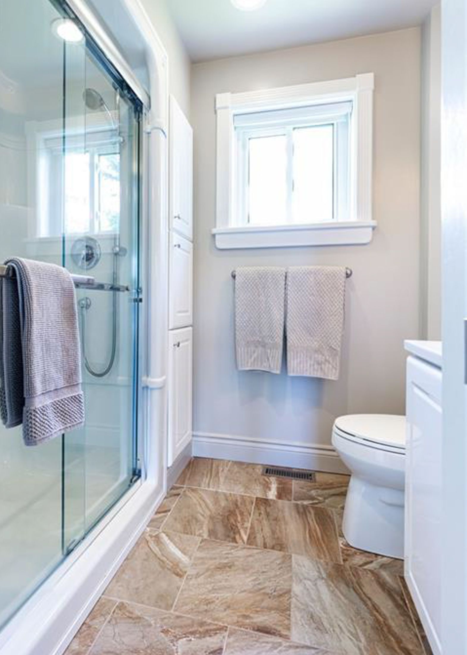 Modern bathroom with glass shower enclosure, white fixtures, and brown marble-look tile flooring.