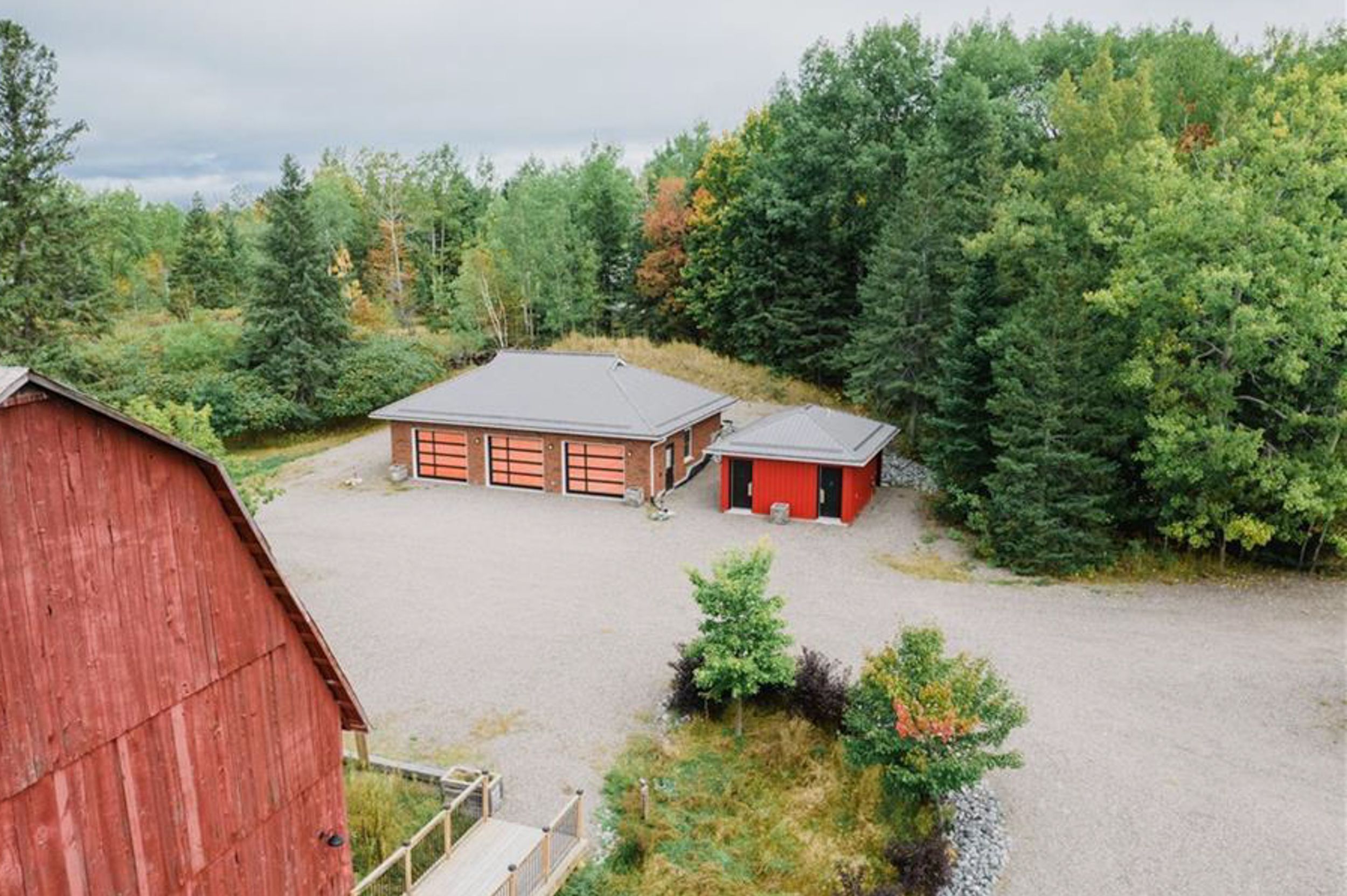 Red barn and outbuildings surrounded by fall foliage and gravel parking area viewed from above.