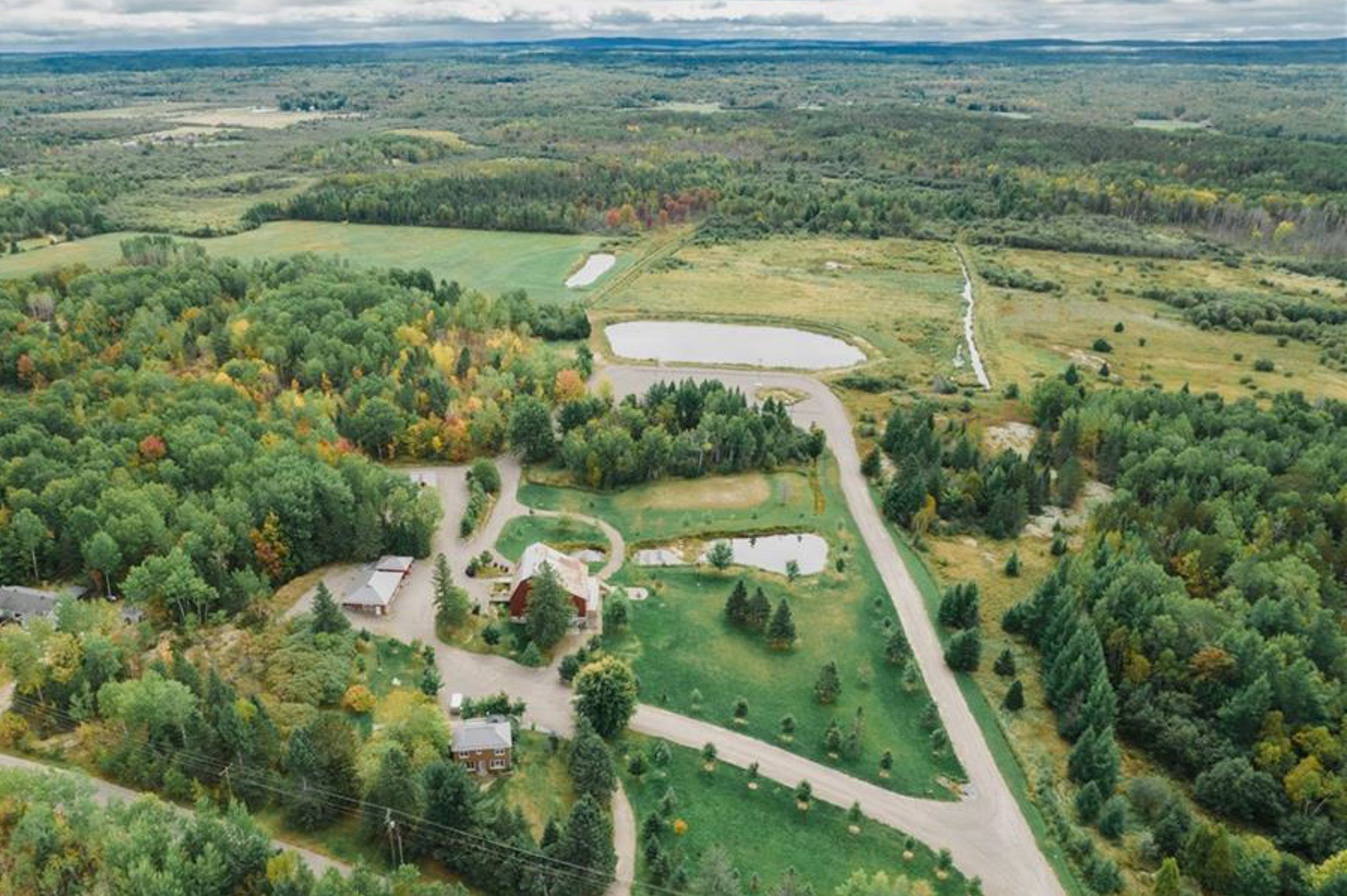 Drone shot of rural property with buildings and roads nestled in colorful autumn forest.
