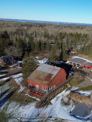 Aerial view of a rustic red building with metal roof surrounded by snowy forest landscape.